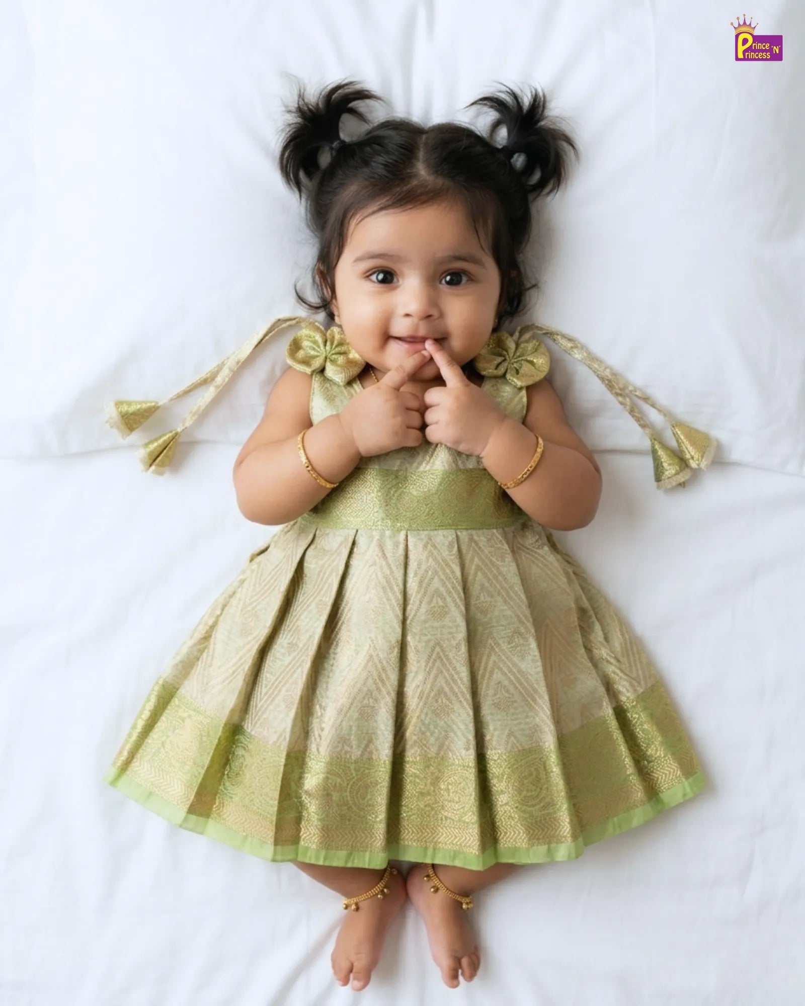 Baby in a green dress lying on a white surface