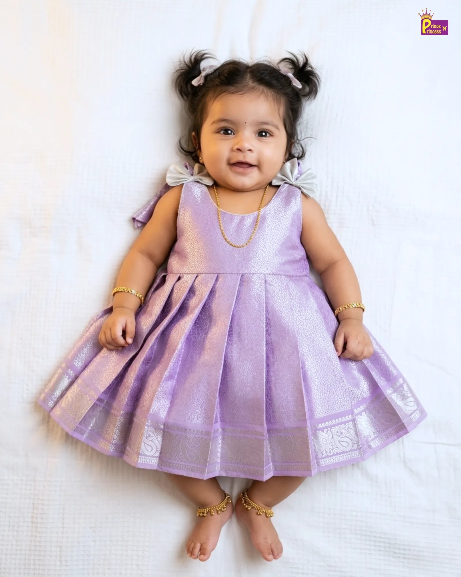 Baby in a purple dress lying on a white surface