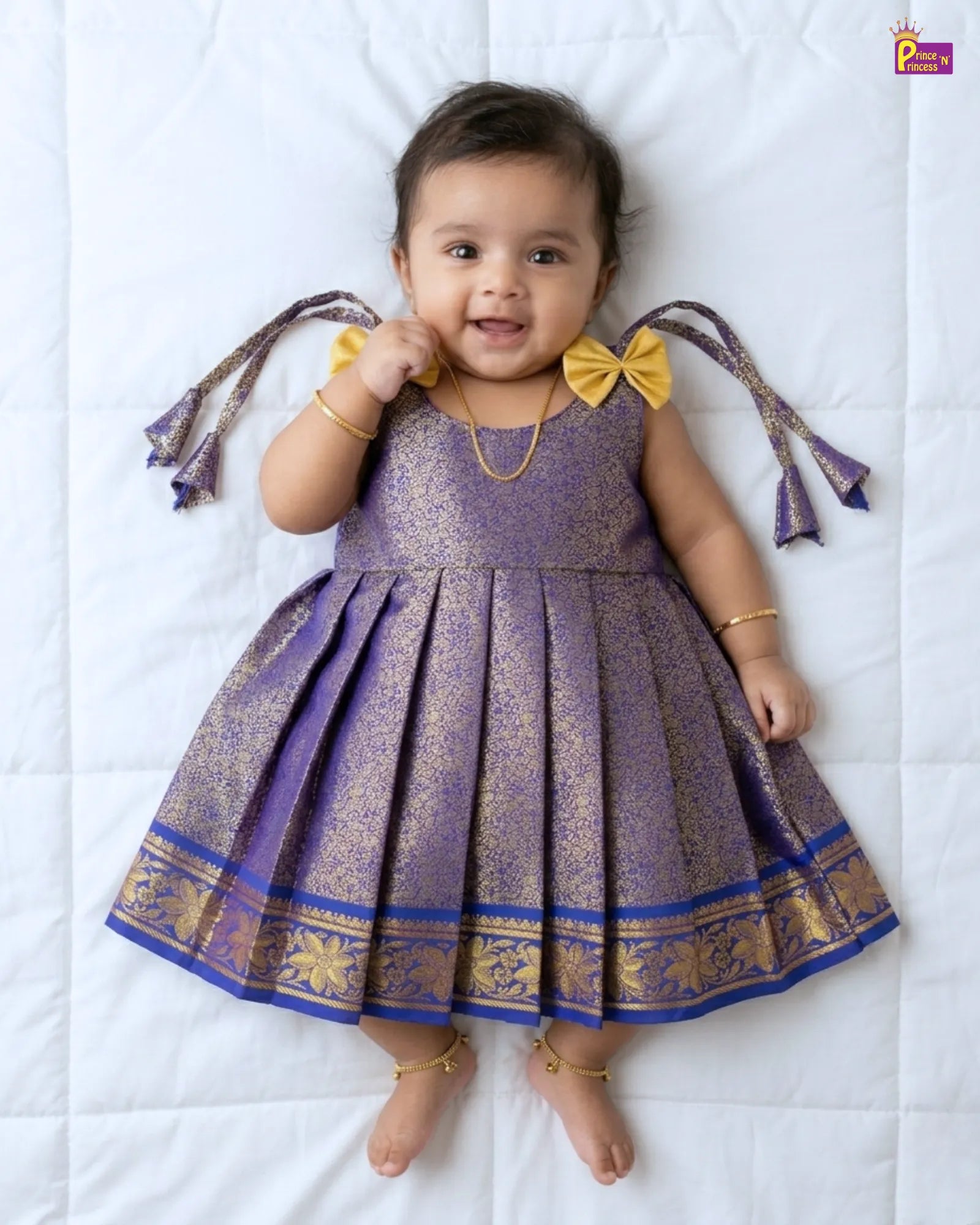 Baby wearing a purple and gold dress with decorative elements on a white background