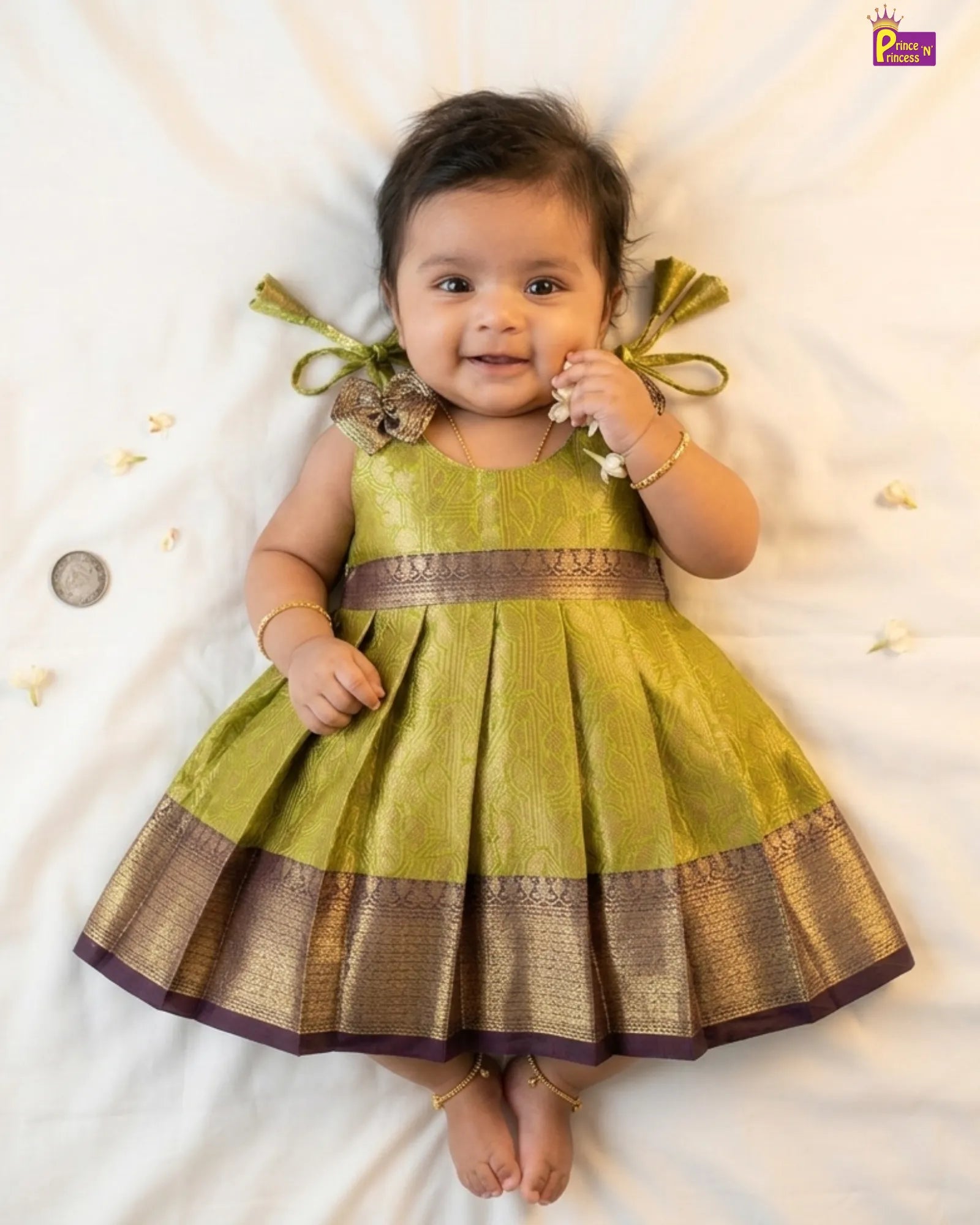 Baby wearing a green traditional dress with gold accents on a white background