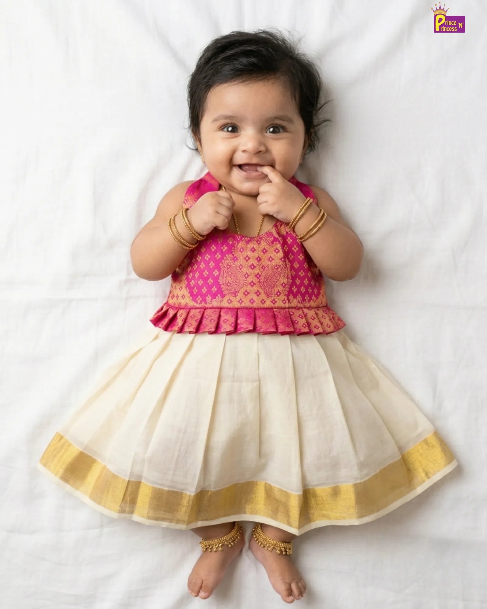 Baby wearing a pink and white traditional outfit with gold accents on a white background