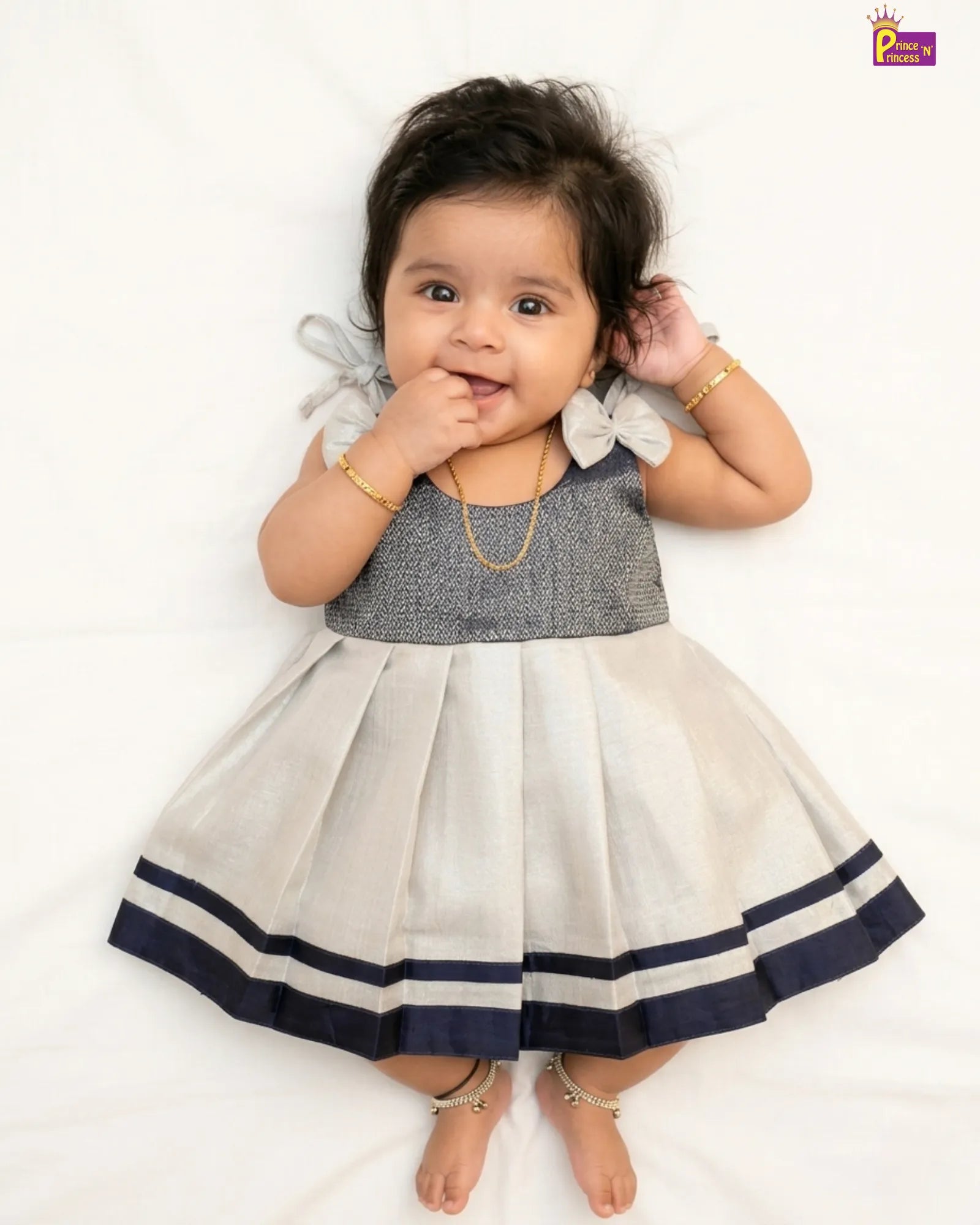 Baby wearing a gray and white dress with blue trim on a white background