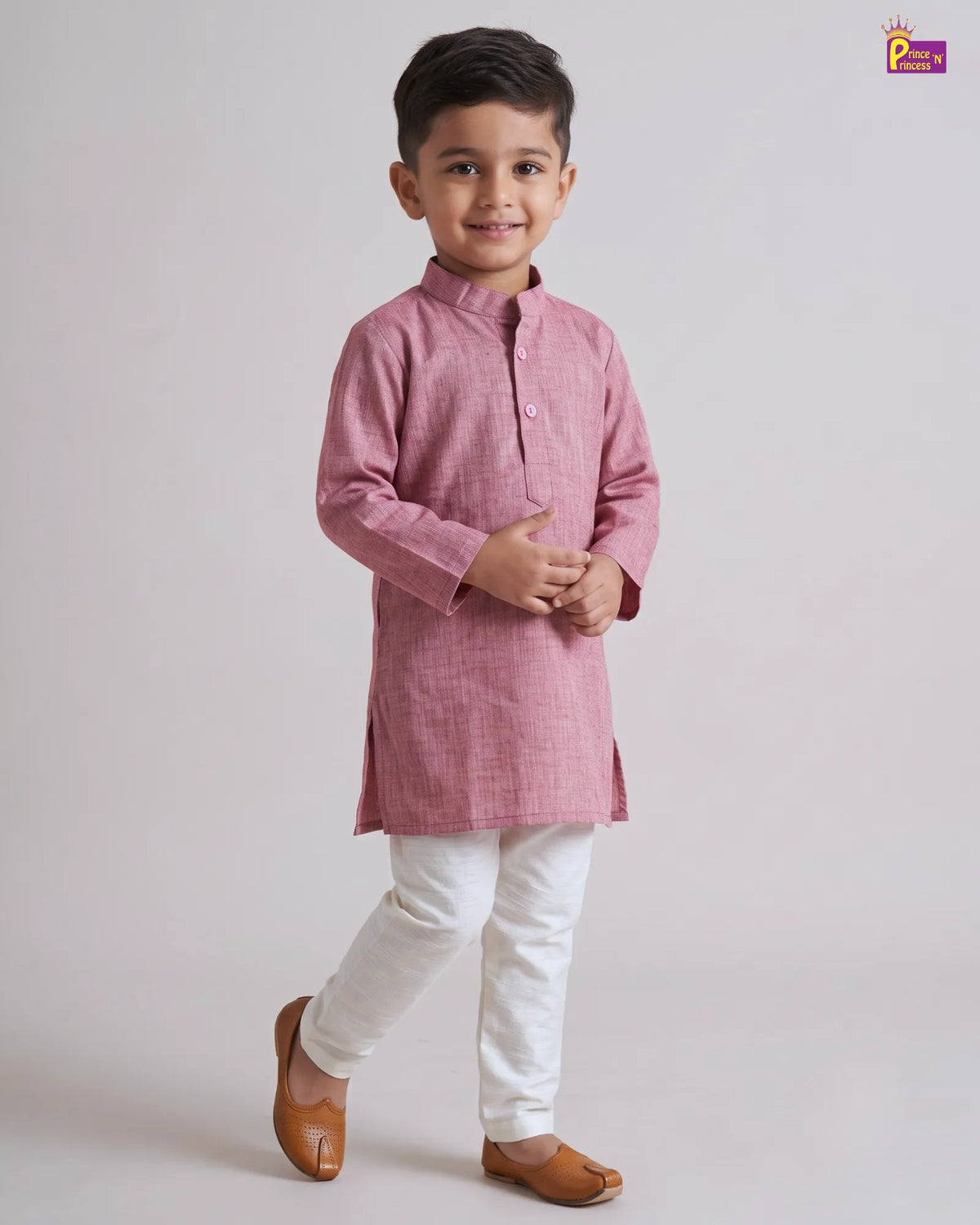 A young boy modeling a pink long-sleeve kurta with white pants and brown leather shoes, standing against a light gray studio background.