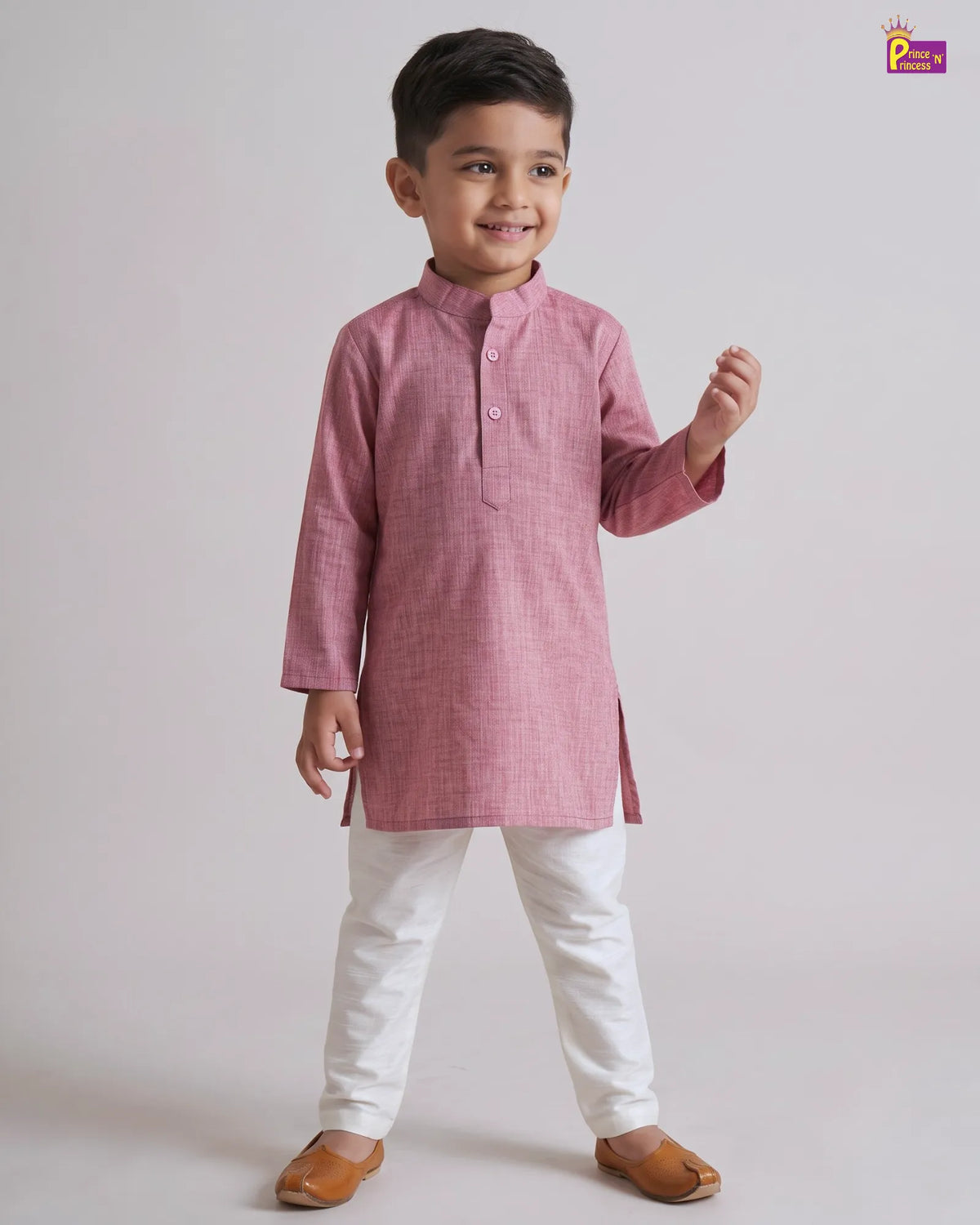 A young boy modeling a pink textured kurta with white pants and brown sandals, standing against a light gray studio background.