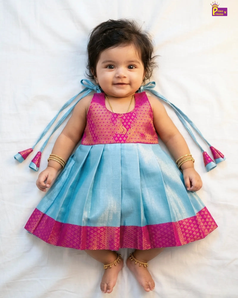 Baby wearing a pink and blue traditional outfit with decorative elements on a white background