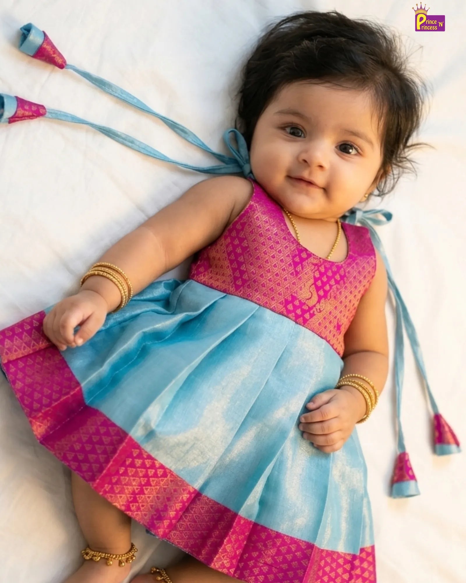 Baby wearing a colorful traditional outfit with pink and blue patterns on a white background
