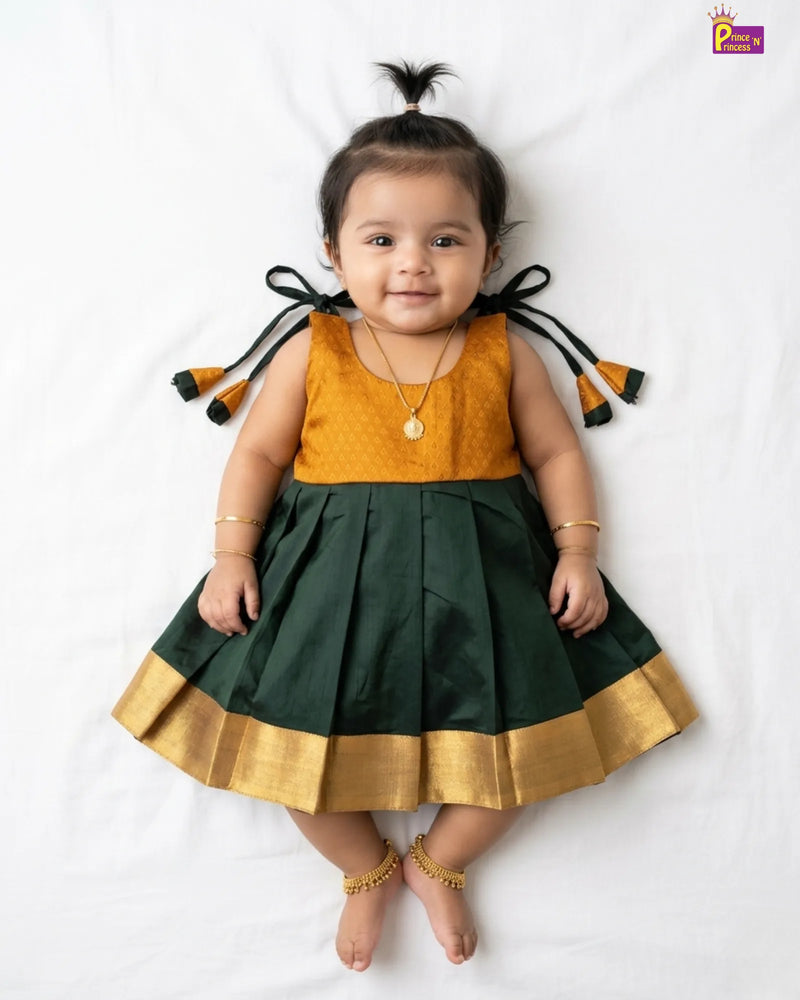 Baby wearing a green and mustard dress with tassels on a white background