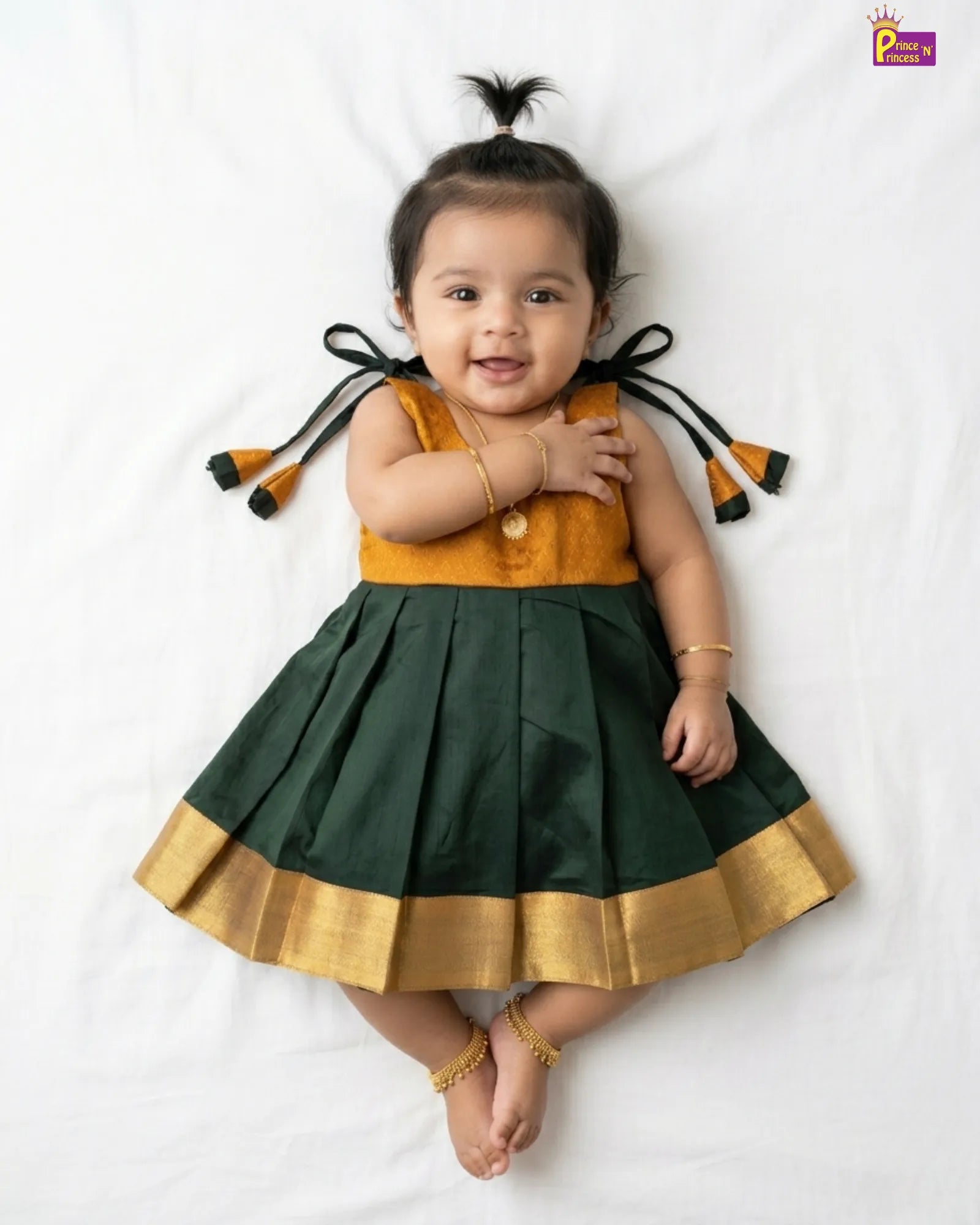 Baby wearing a green and mustard traditional outfit with decorative elements on a white background