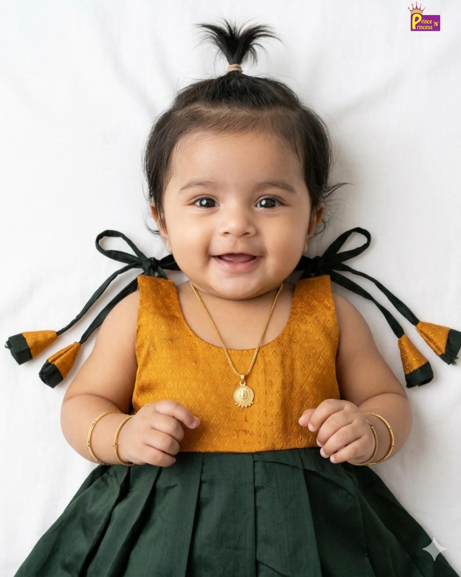 Baby wearing a mustard yellow top and green skirt with decorative ribbons on a white background