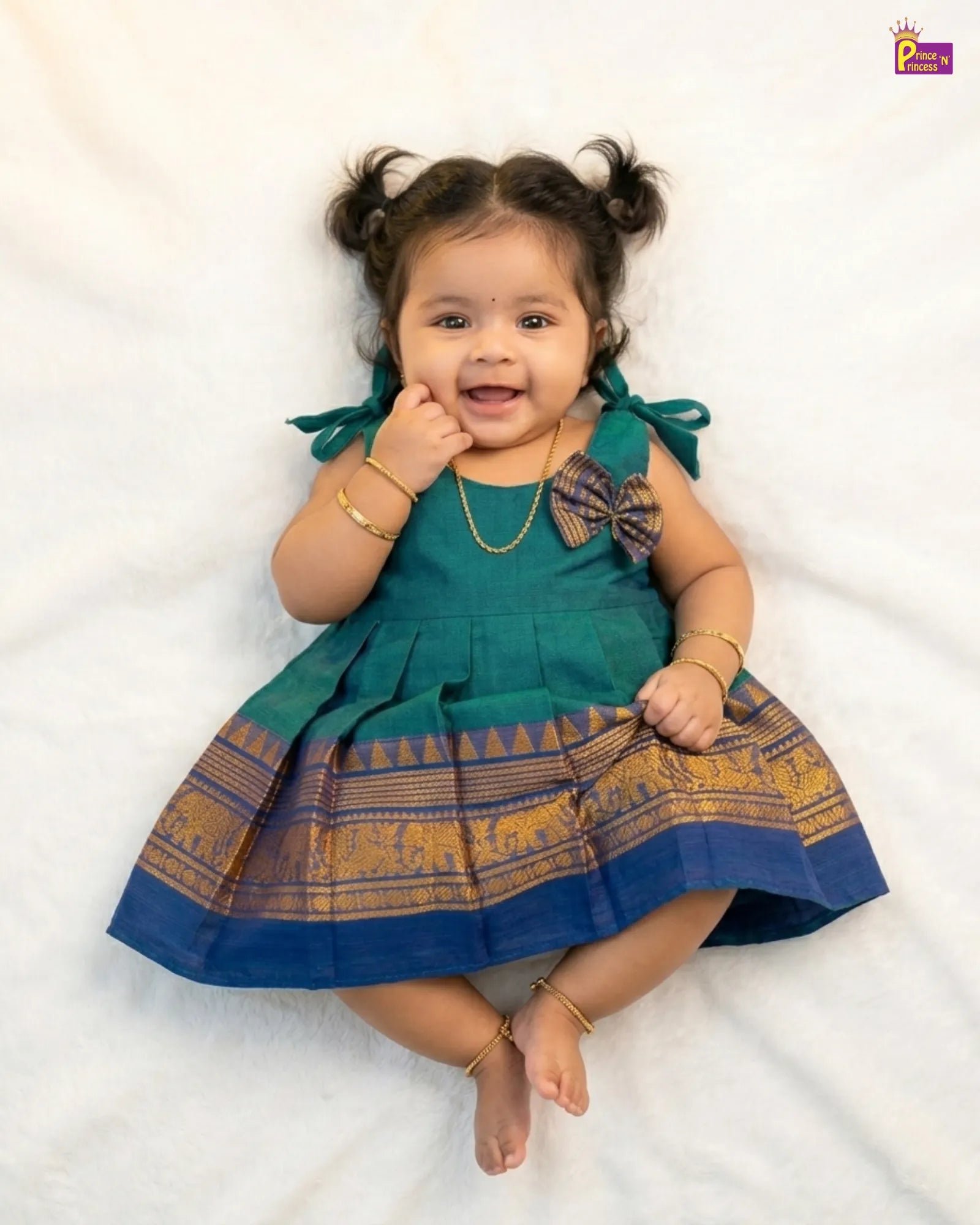 Baby wearing a green and blue traditional outfit with elephant patterns on a white background