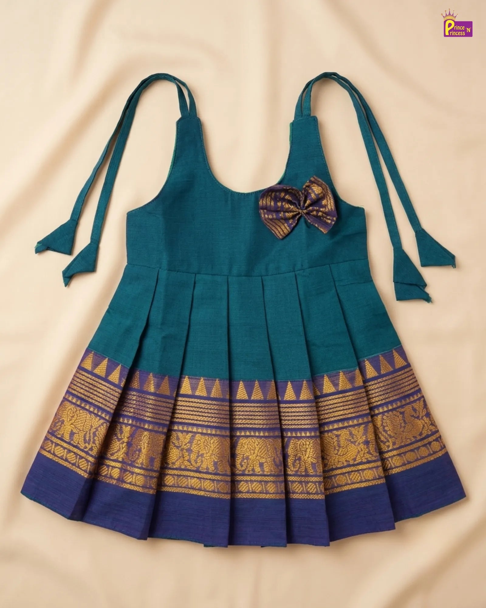 Teal dress with gold elephant patterns and a purple bow on a beige background