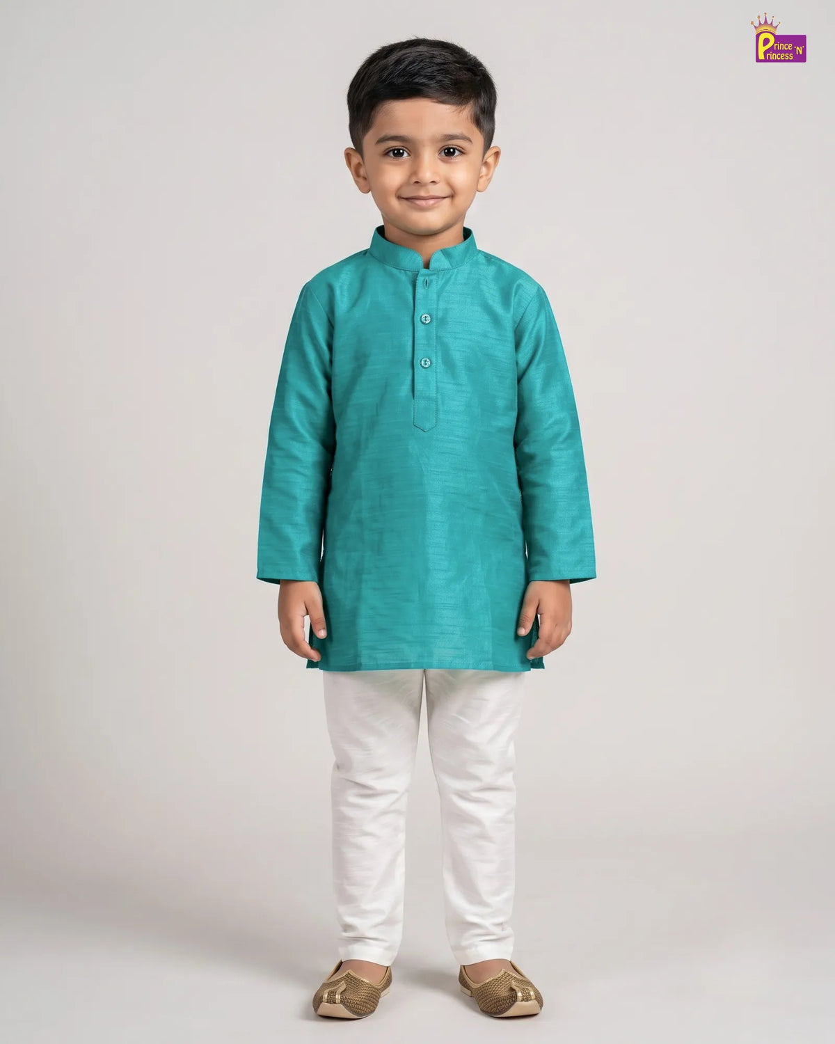 A young boy modeling a teal green long-sleeve kurta with white trousers and brown shoes, standing against a light gray studio background.