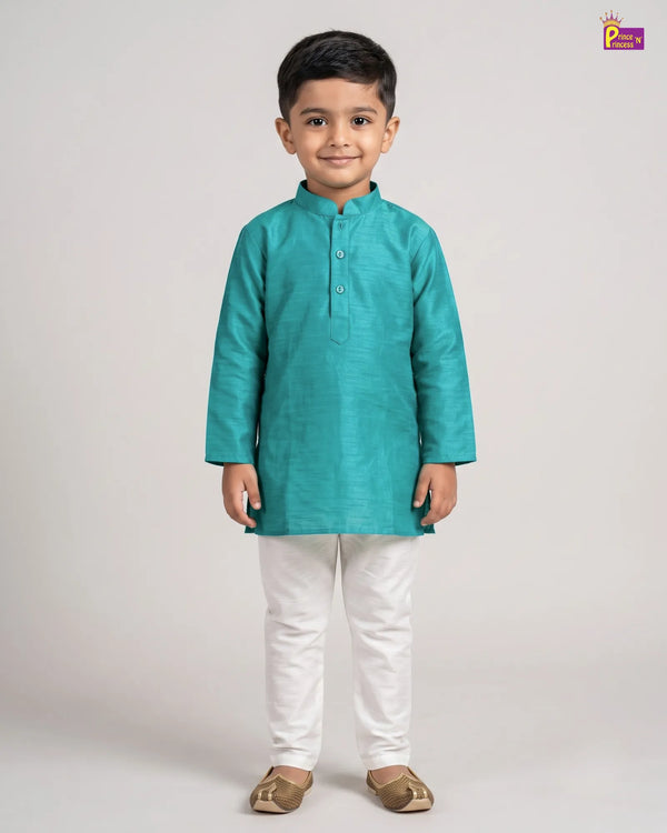 A young boy modeling a teal green long-sleeve kurta with white trousers and brown shoes, standing against a light gray studio background.