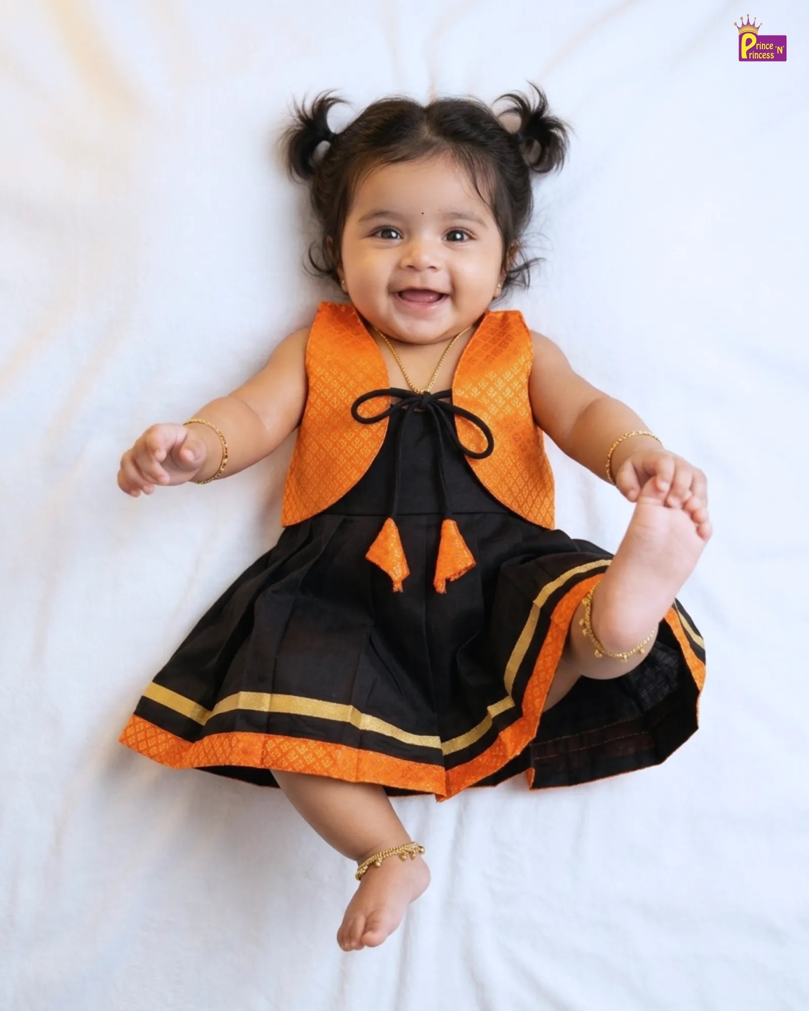Baby wearing an orange and black dress on a white background