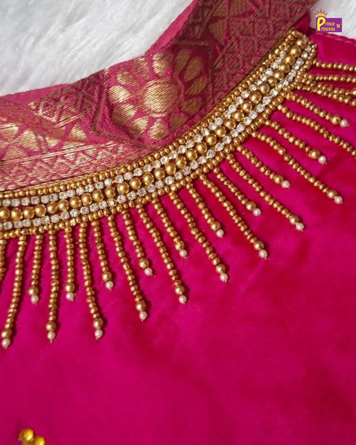 Close-up of a bright pink fabric garment with an ornate gold brocade yoke and a wide beaded neckline featuring dangling gold bead strands.