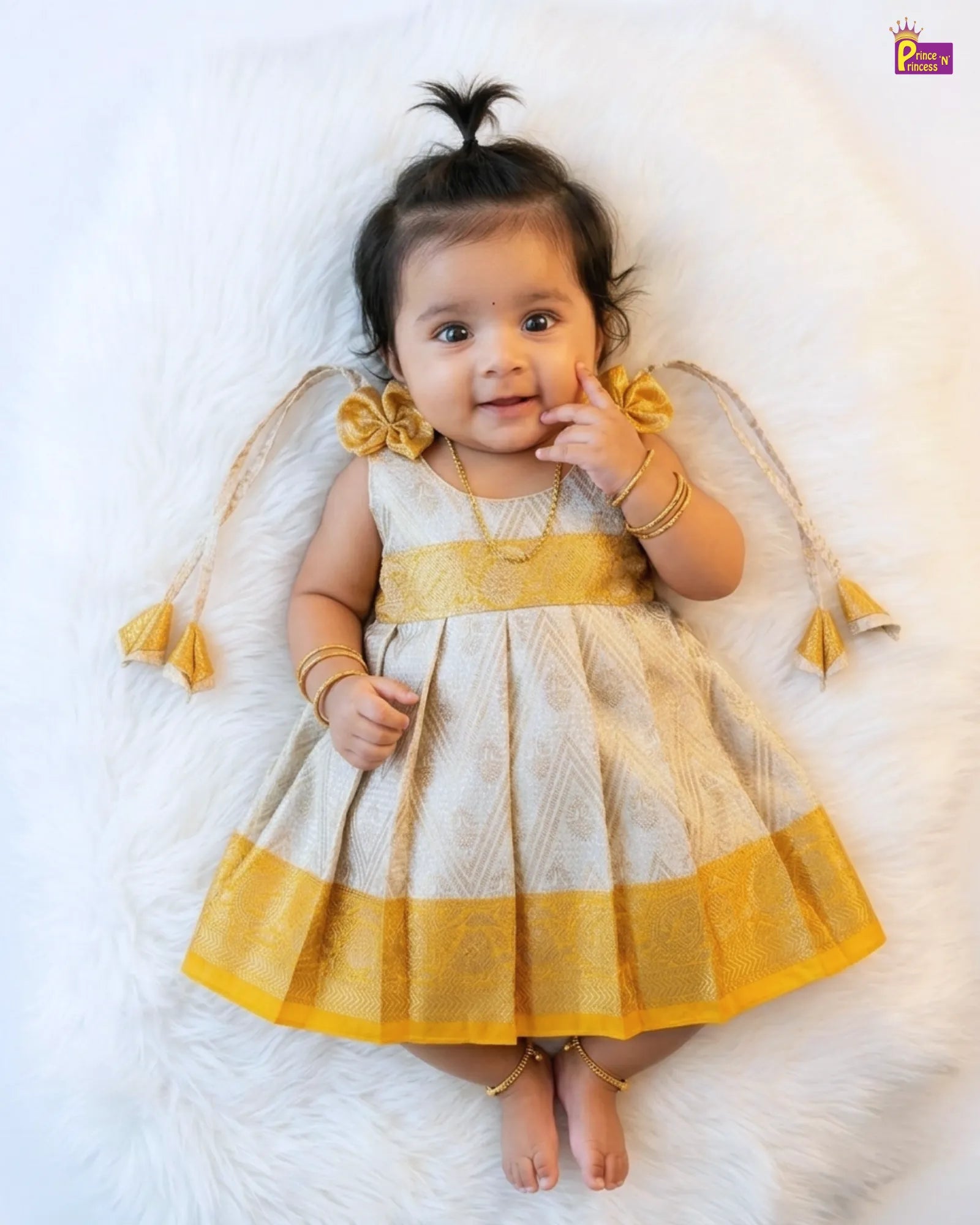 Baby wearing a yellow and white dress with tassels on a white background
