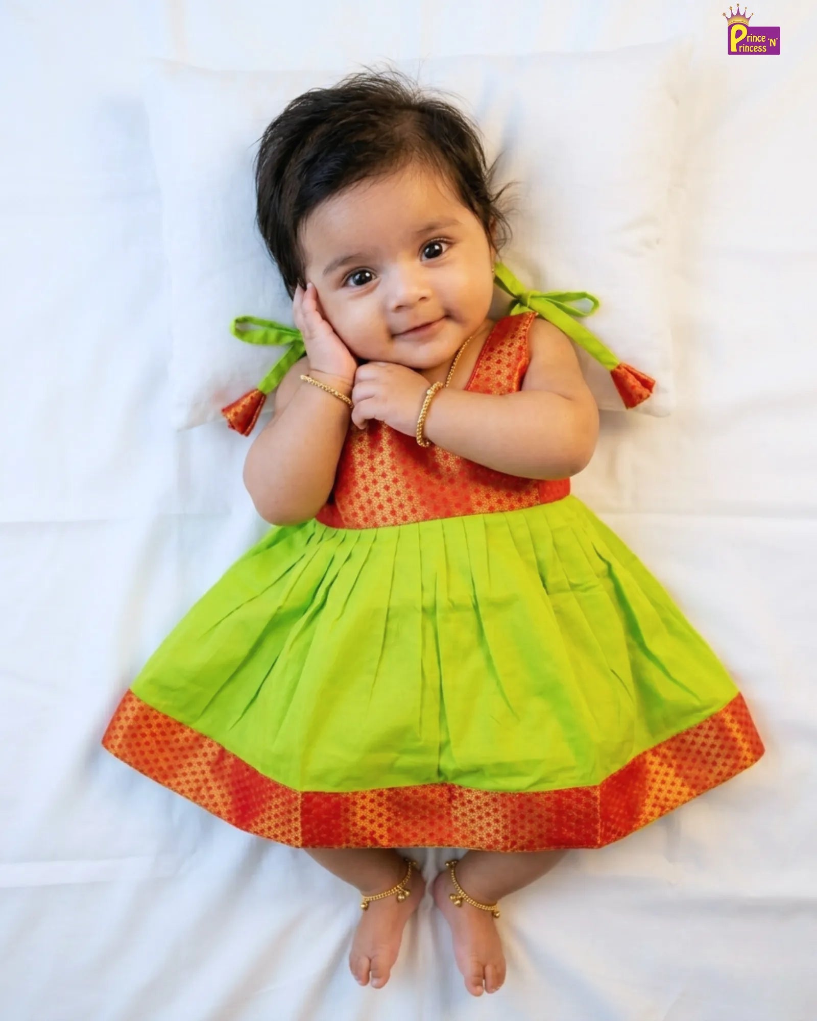 Baby wearing a colorful dress lying on a white surface