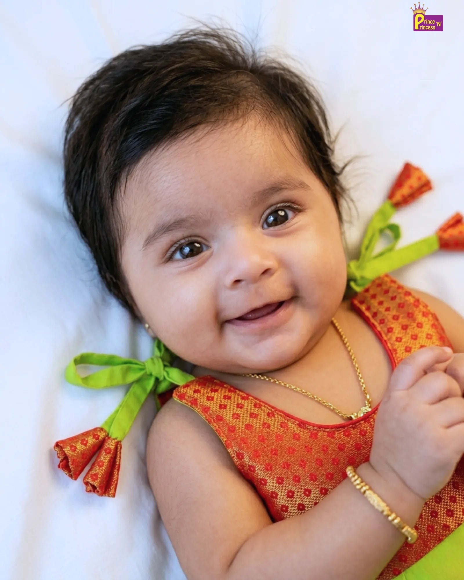 Baby in an orange outfit with green ribbons on a white background