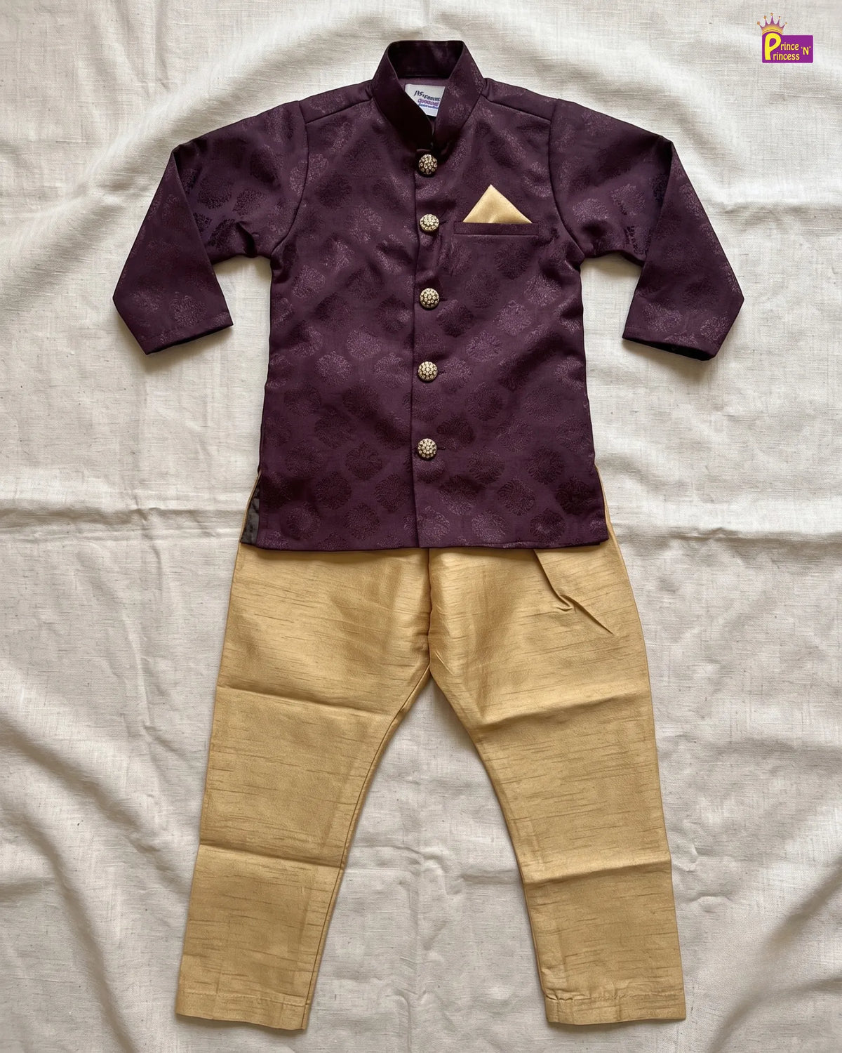 A two-piece boys' traditional outfit laid flat on a white fabric background, featuring a dark purple embroidered long-sleeve jacket with gold buttons and a matching gold pocket square, paired with gold trousers.
