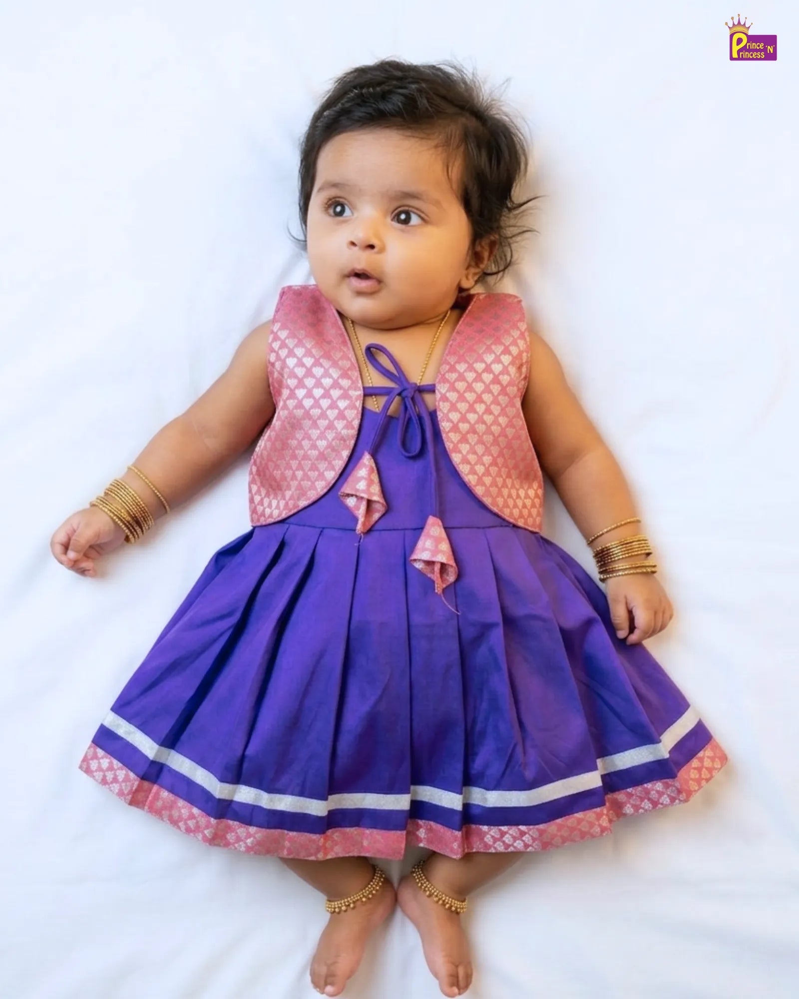 Baby wearing a purple dress with pink accents on a white background