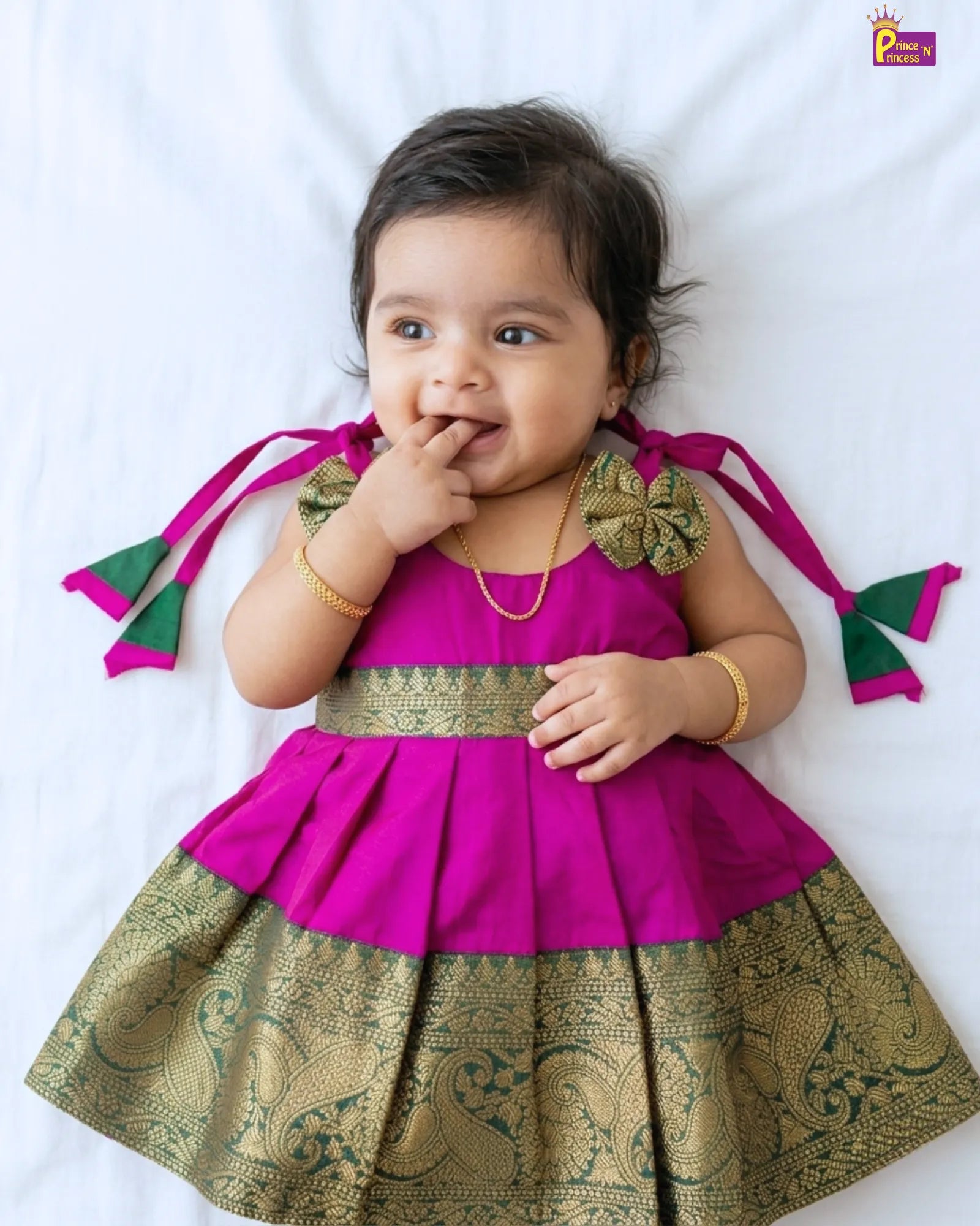 Baby wearing a pink and green traditional outfit on a white background