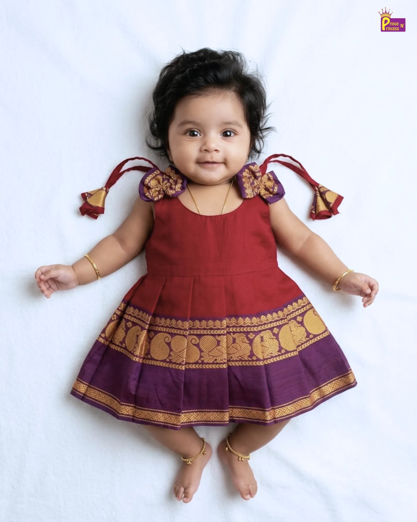 Child wearing a red and purple traditional outfit with gold patterns on a white background
