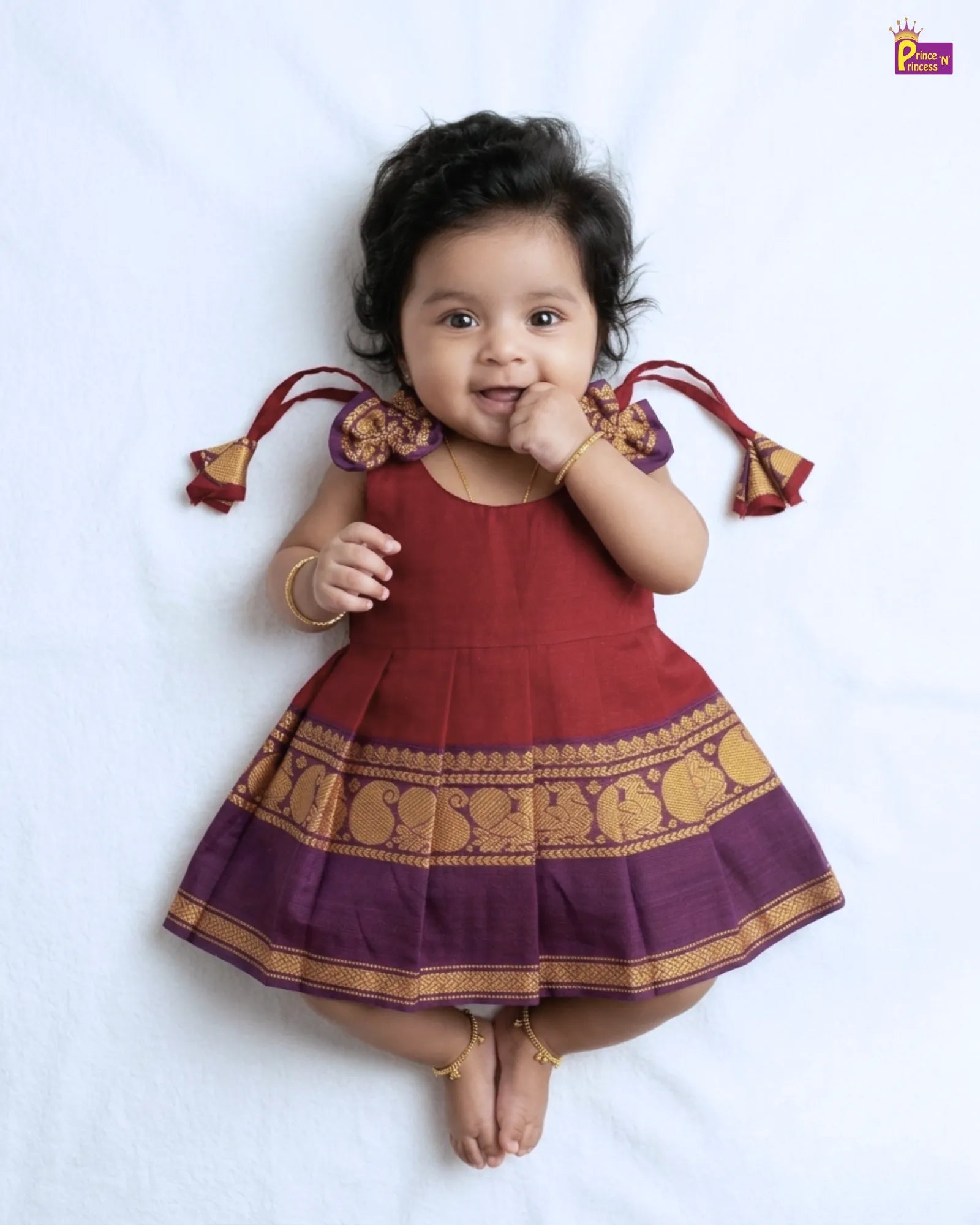 Baby wearing a traditional outfit with a red and purple color scheme on a white background