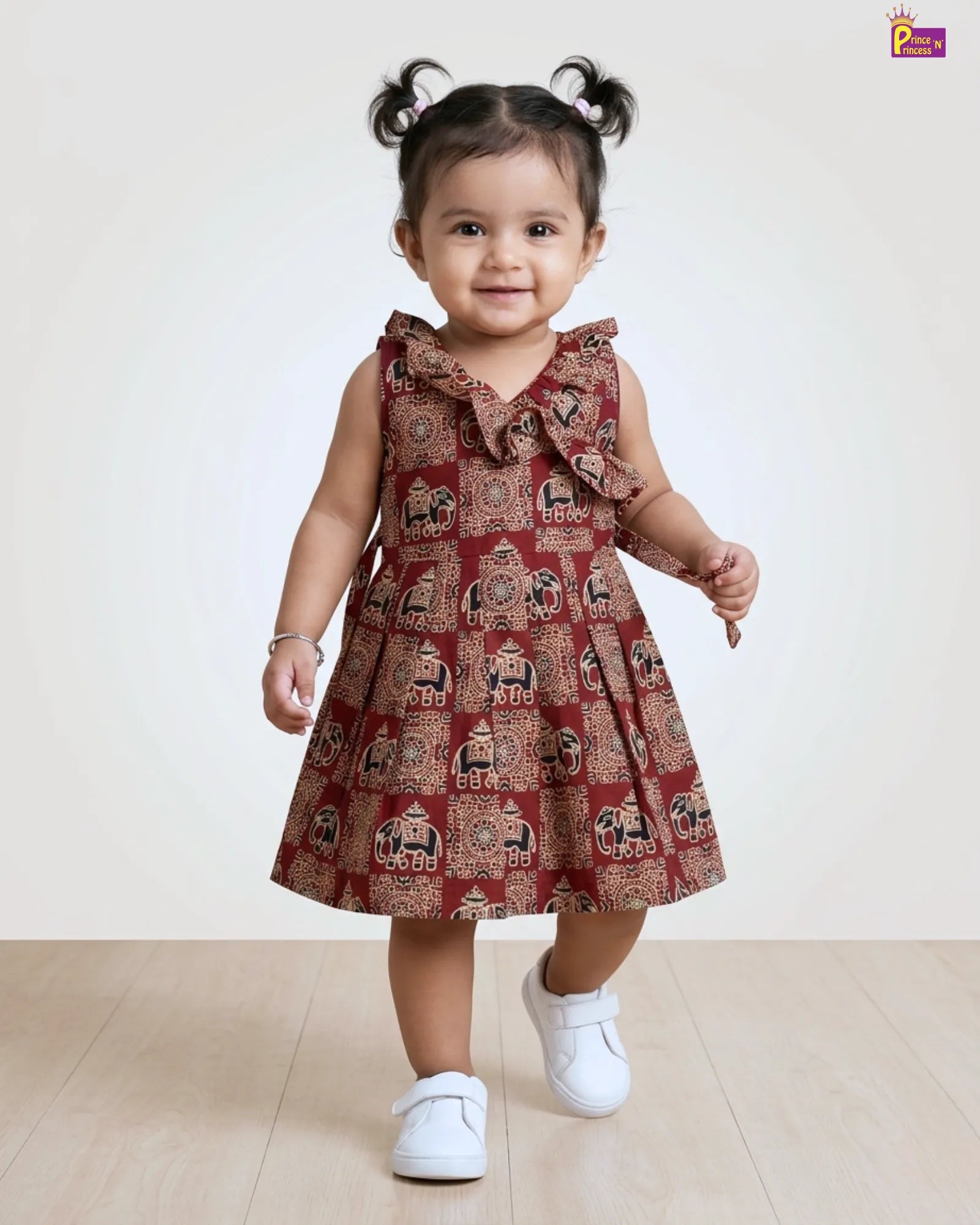 Child wearing a red patterned dress with white shoes on a beige background