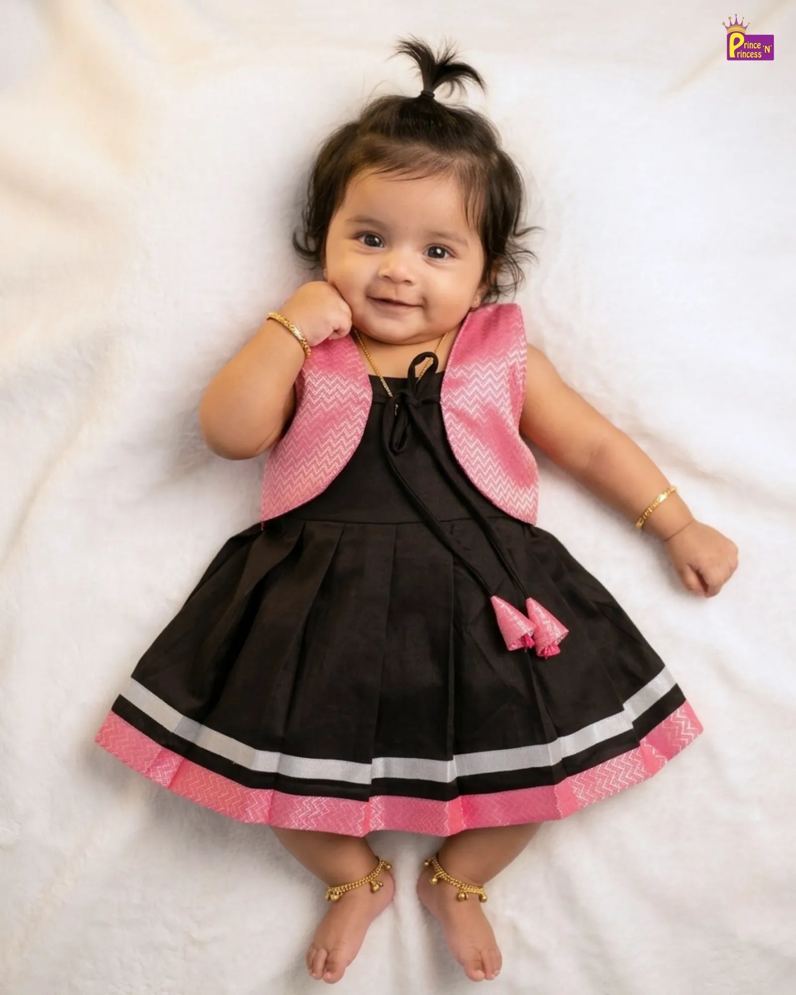 Baby wearing a black and pink dress with a matching jacket on a white background