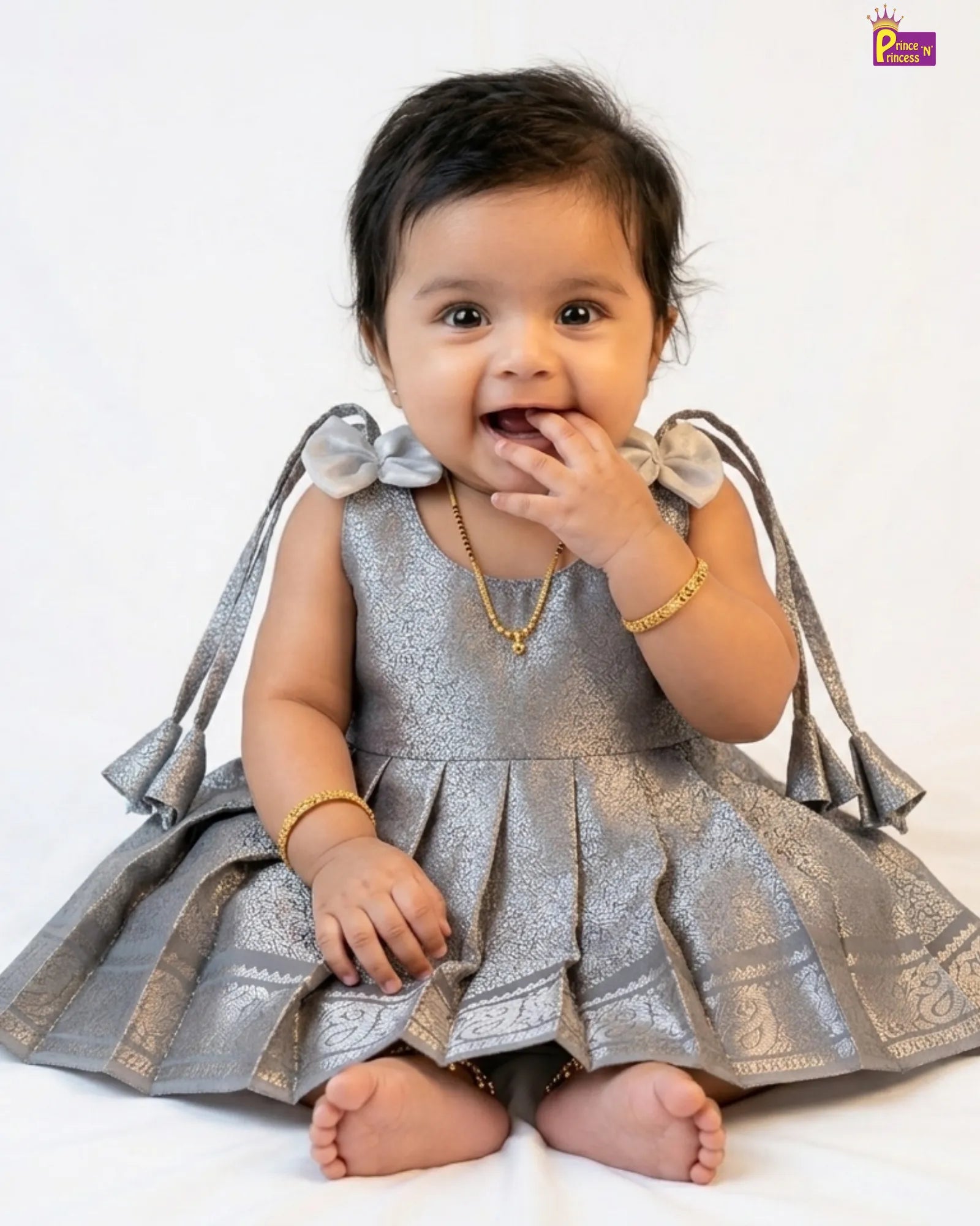 Baby wearing a silver dress with decorative elements on a white background