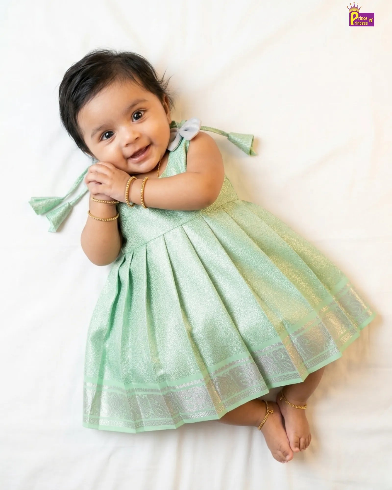 Baby in a light green dress lying on a white surface