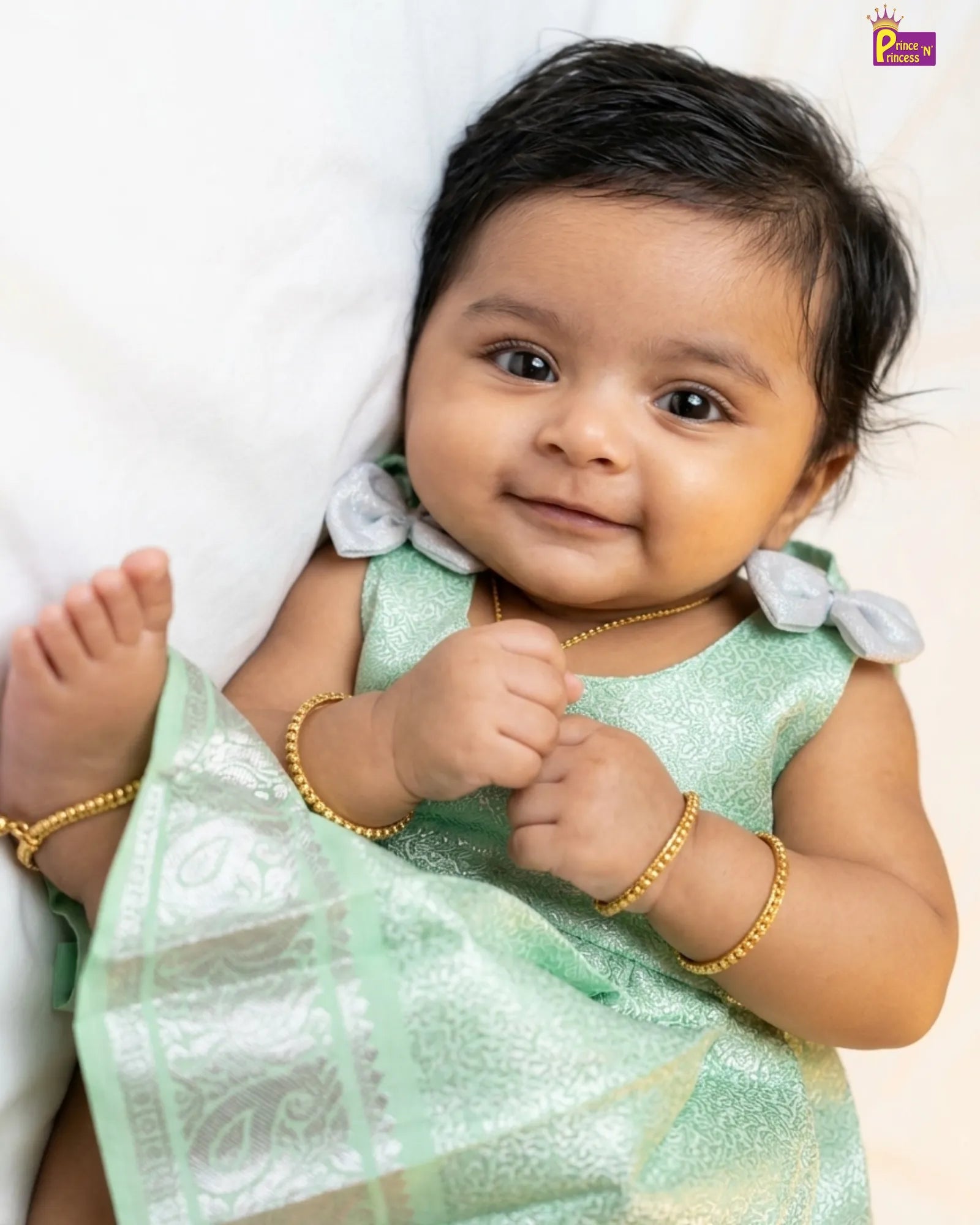 Baby in a light green traditional outfit with gold jewelry on a white background