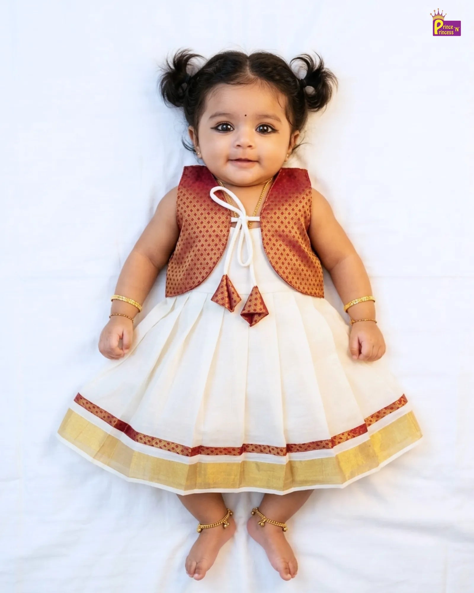 Baby wearing a white dress with red and gold accents on a white background