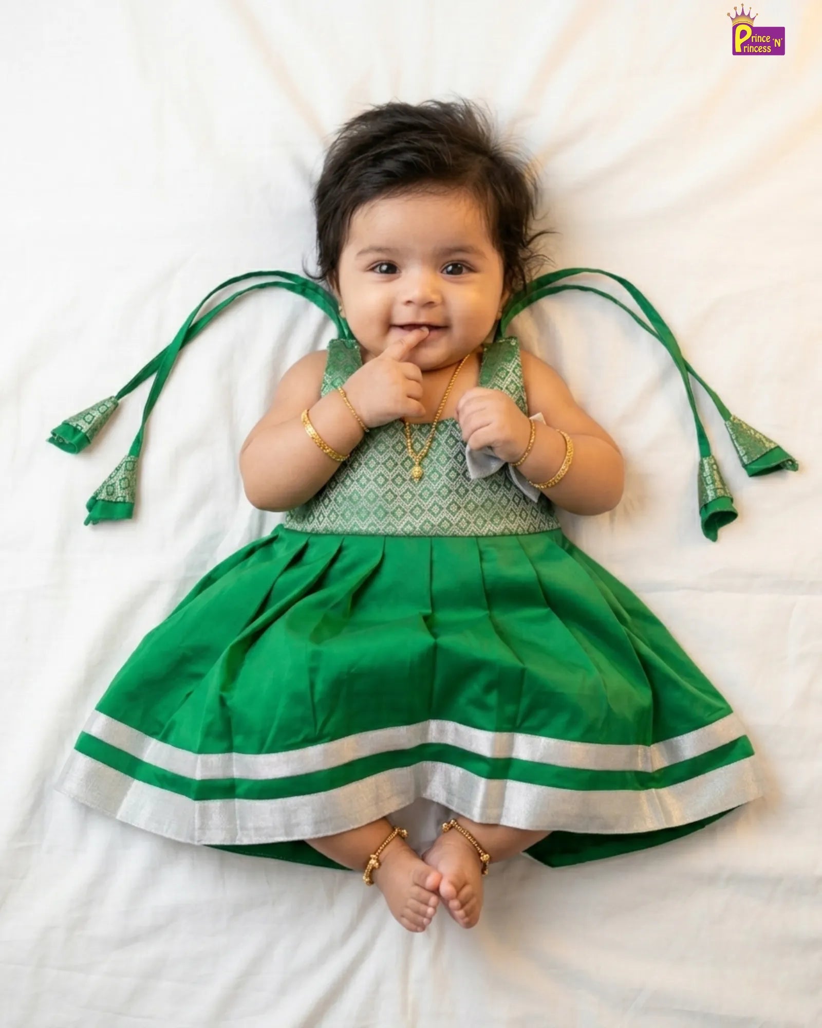 Baby wearing a green traditional outfit with decorative straps on a white background
