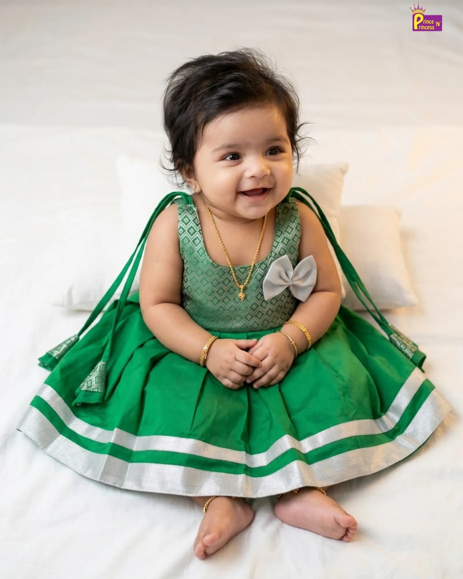 Baby in a green dress with a white bow sitting on a white surface