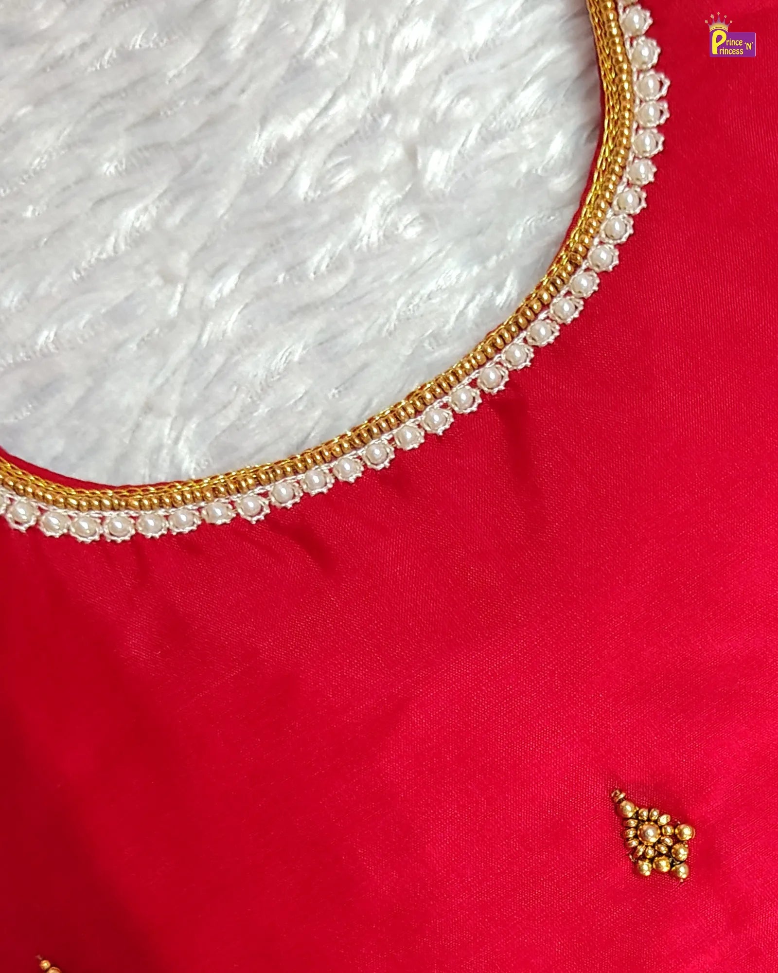Close-up of a red fabric with gold embroidery and pearl detailing.