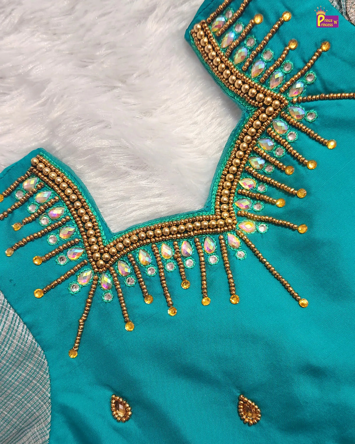 A close-up of a teal blue fabric garment featuring ornate gold beaded embroidery and iridescent rhinestone embellishments around the neckline, with small matching teardrop motifs below.