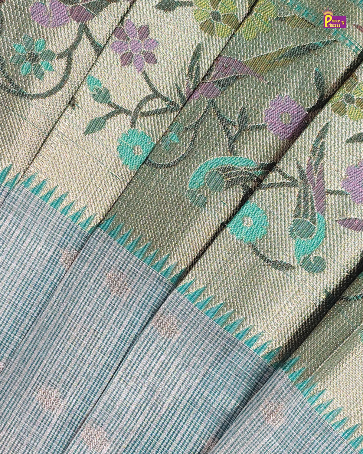 Close-up of a woven textile with a beige and light blue striped body, teal and purple floral motifs, and a decorative border, shown in diagonal folds.