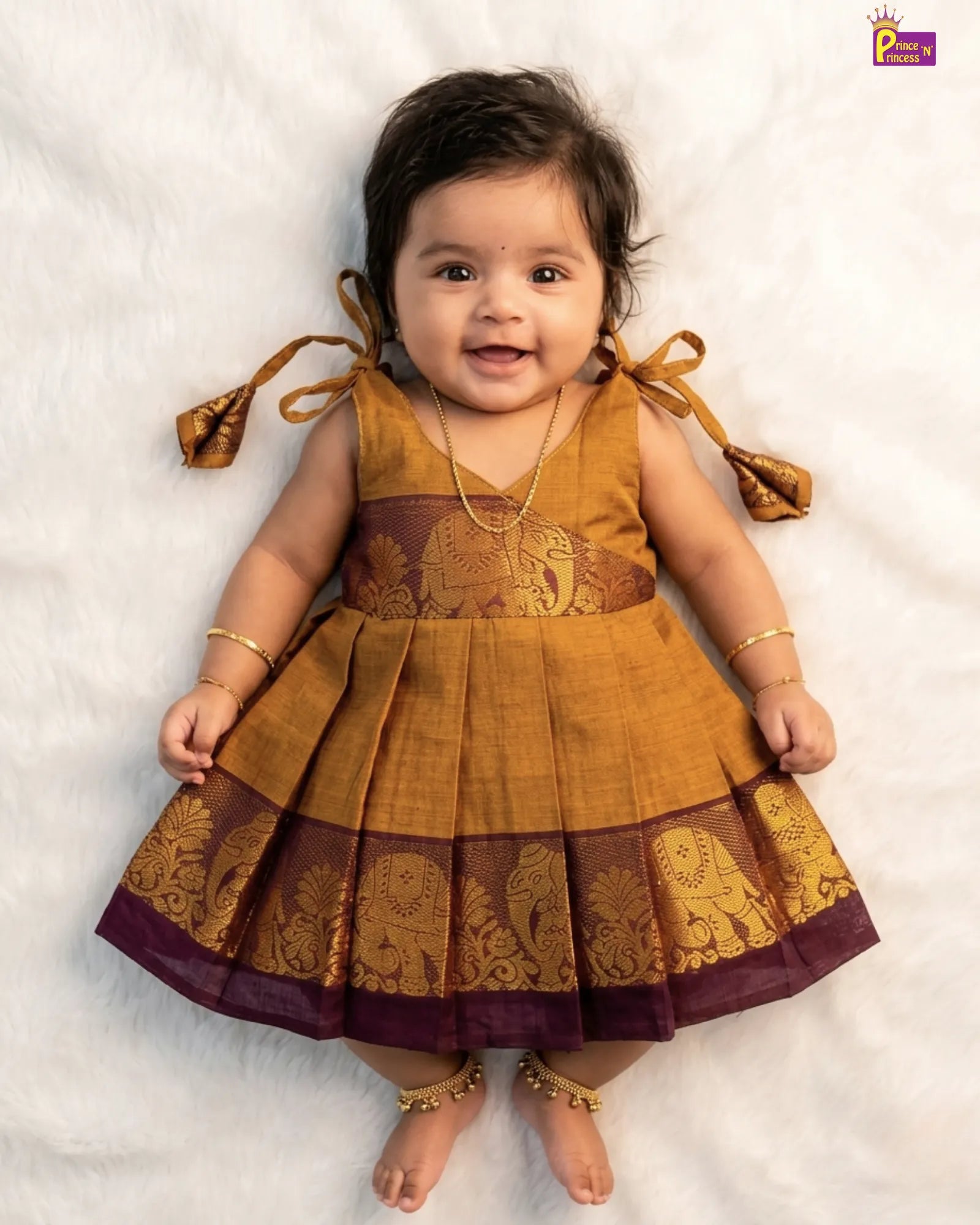 Baby wearing a mustard yellow and brown traditional dress on a white background