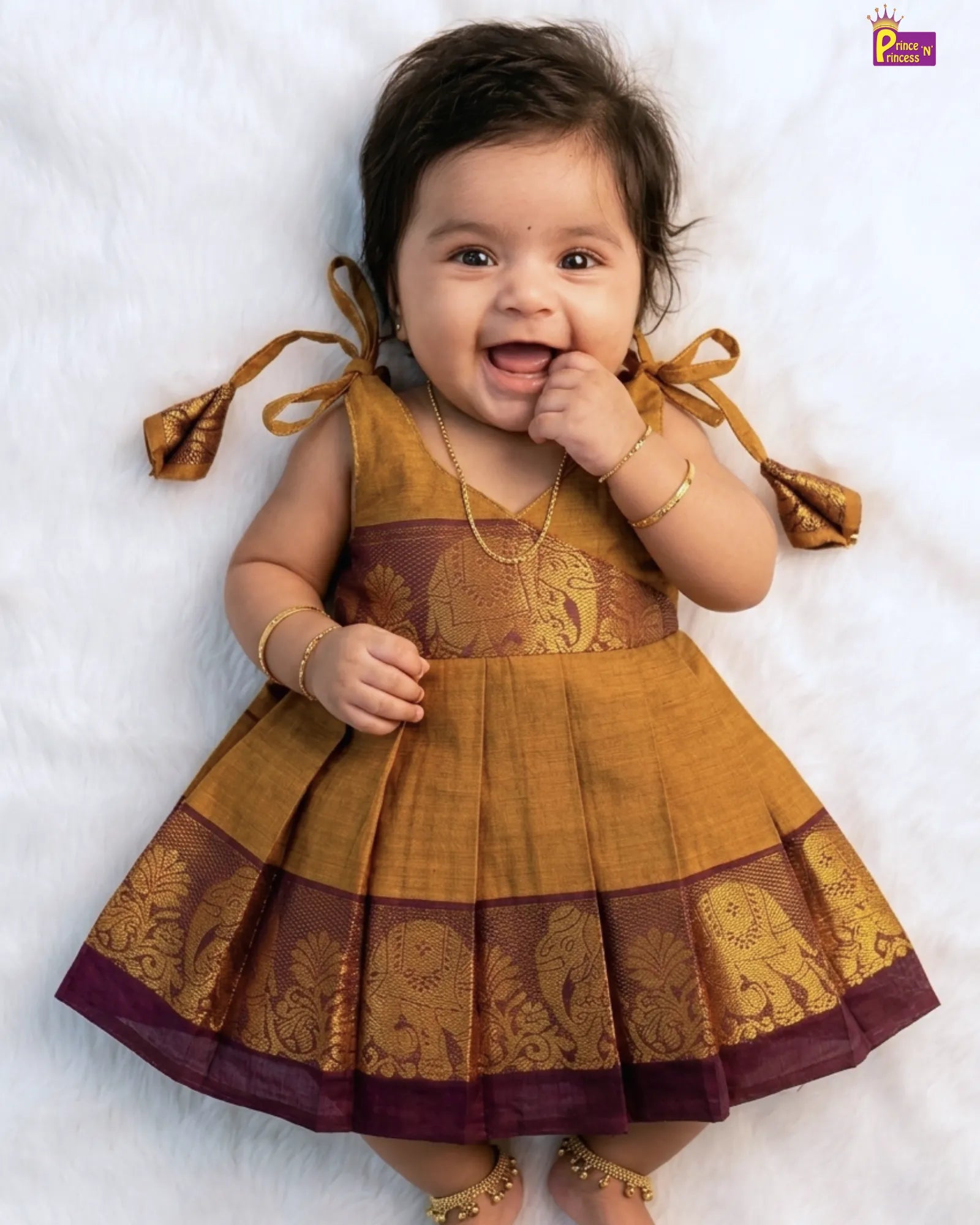 Baby wearing a traditional outfit with gold and brown colors on a white background