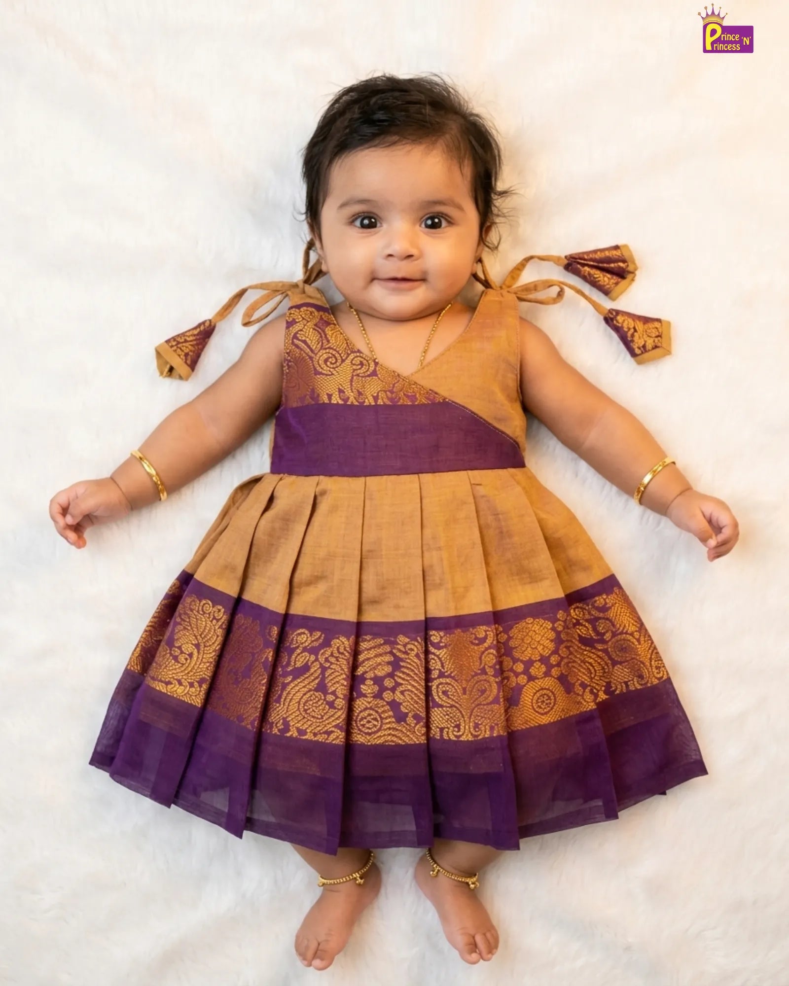Baby wearing a traditional purple and gold dress on a white background