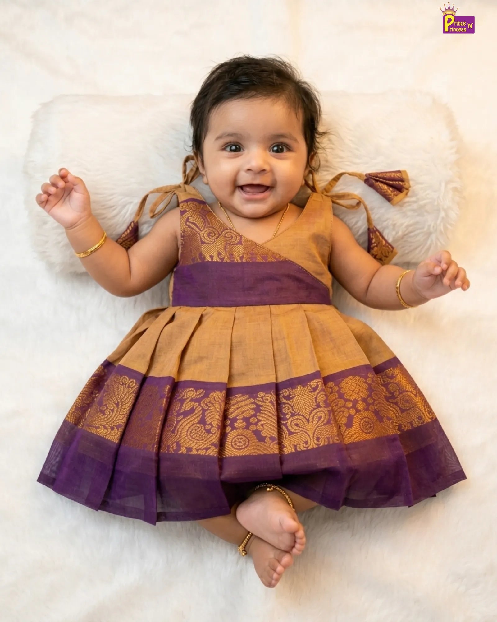 Baby wearing a traditional outfit with purple and gold colors on a white background