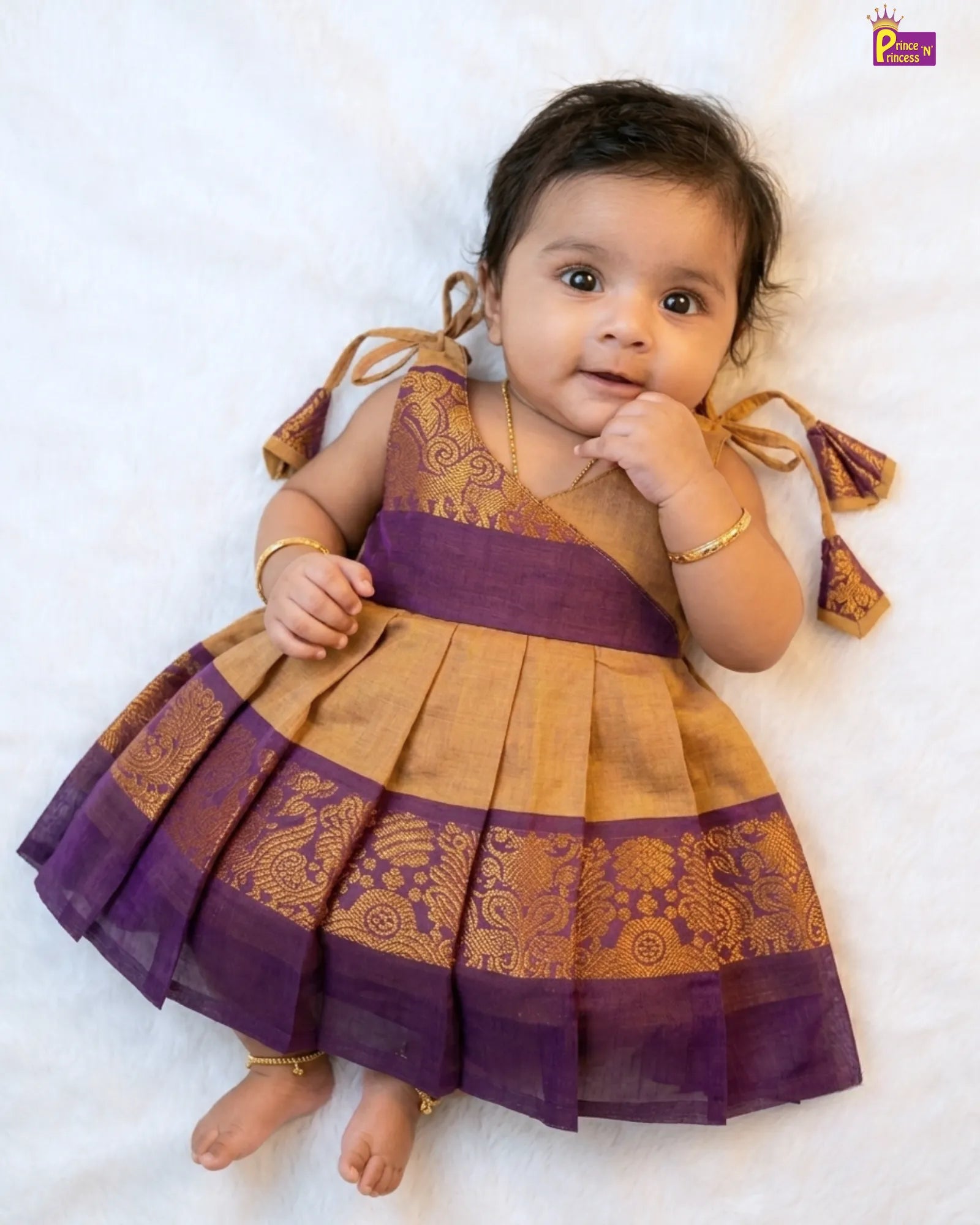 Baby wearing a traditional outfit with purple and gold colors on a white background