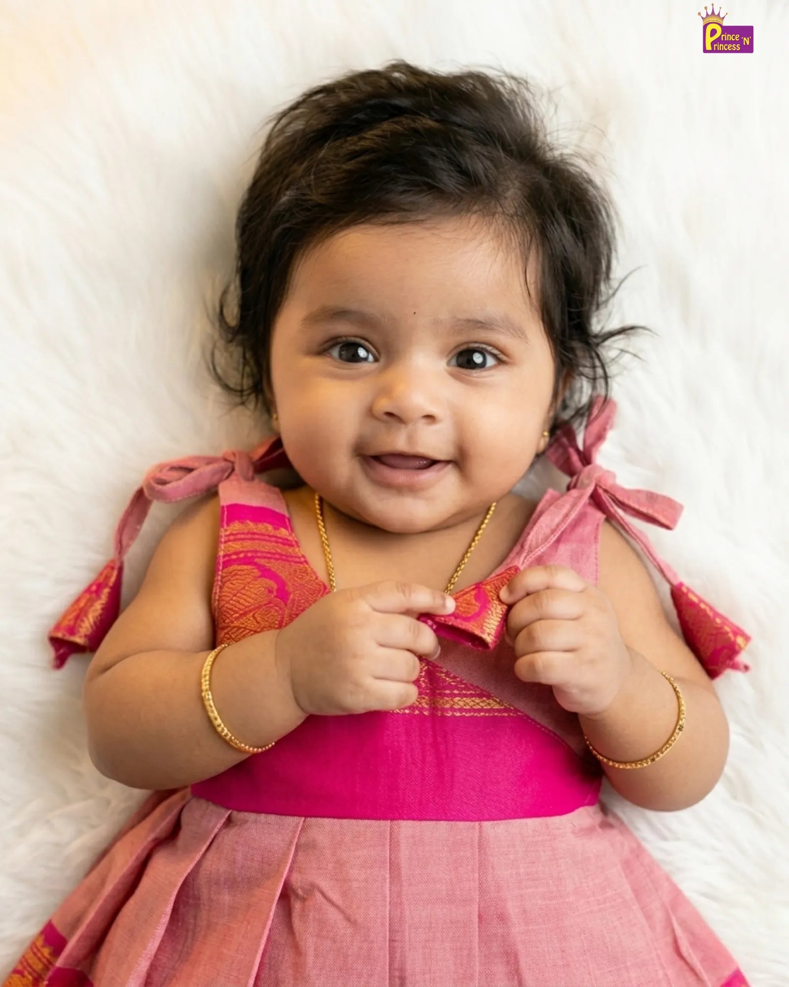 Baby in a pink traditional outfit with gold accents on a white background