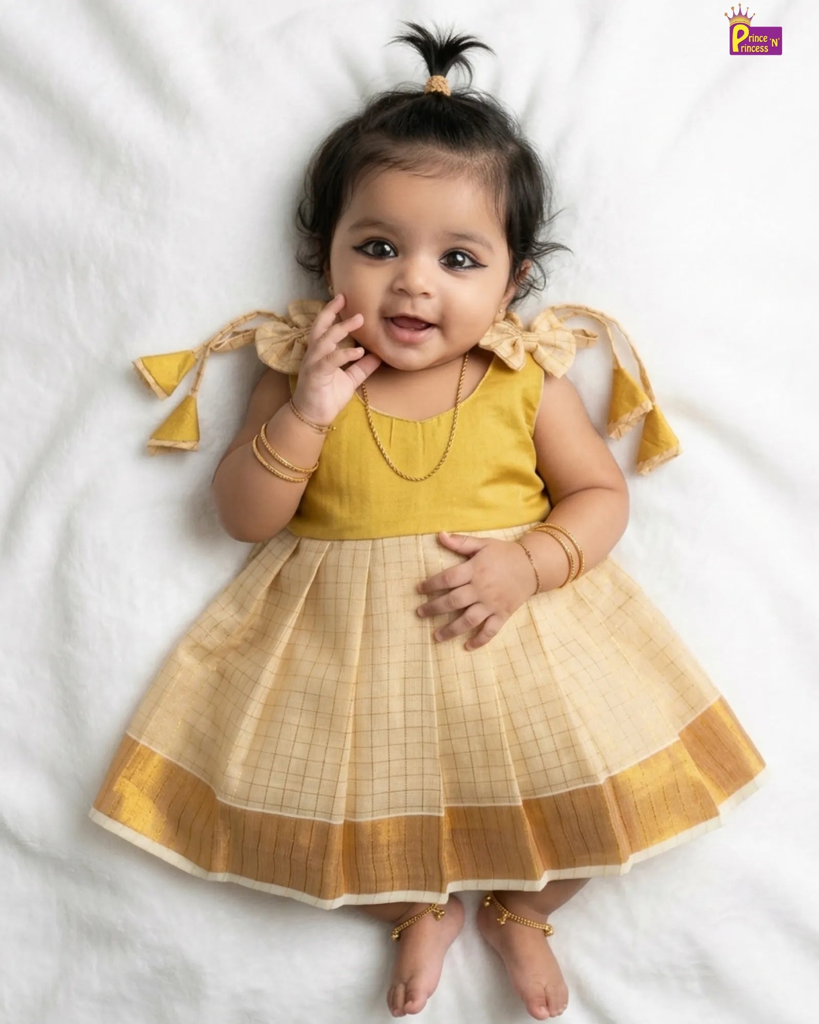 Baby wearing a yellow and beige traditional outfit on a white background