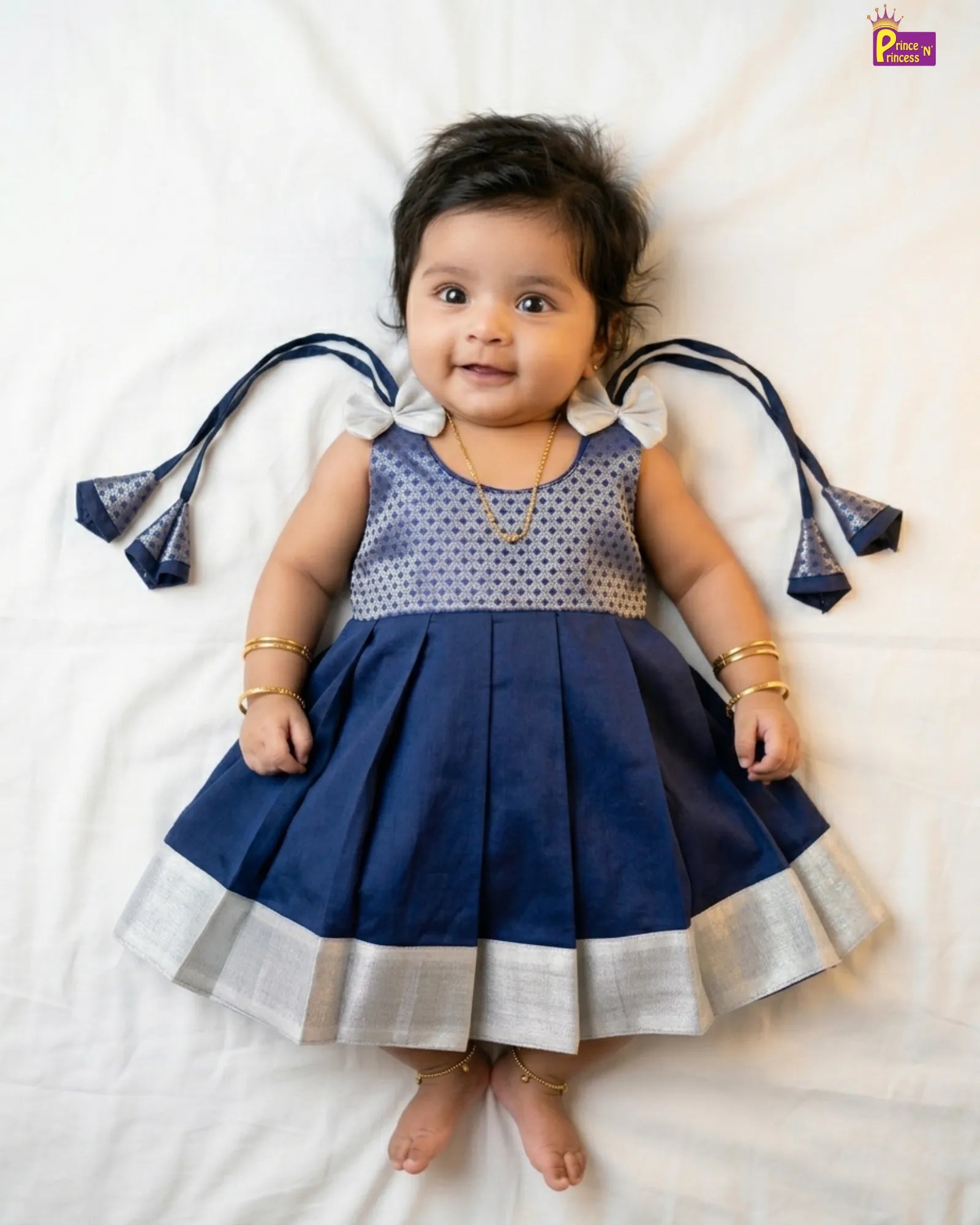 Baby wearing a blue and white dress with decorative ribbons on a white background