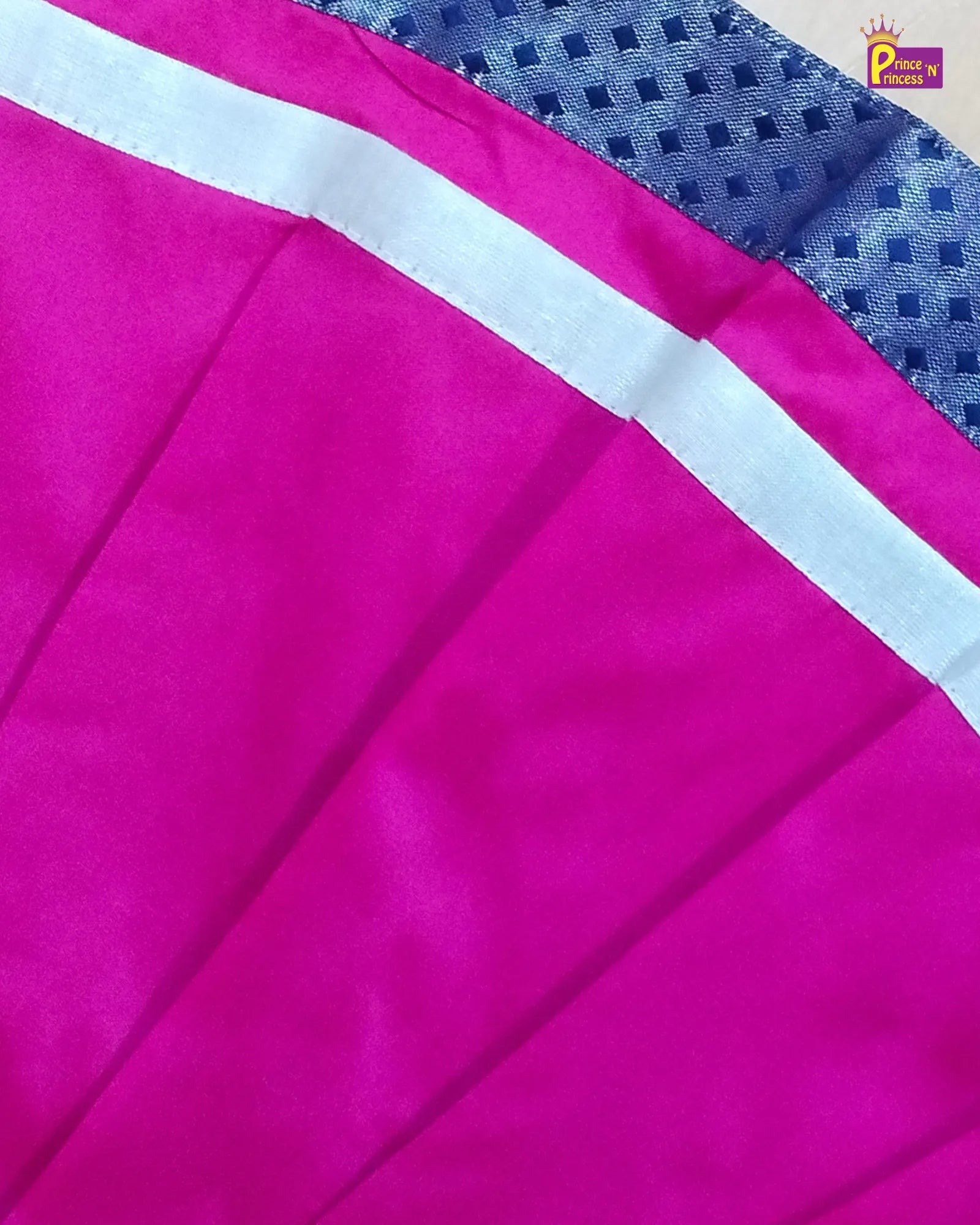 A close-up of a bright pink fabric with a white stripe and a blue patterned border, showing the material texture and folds.