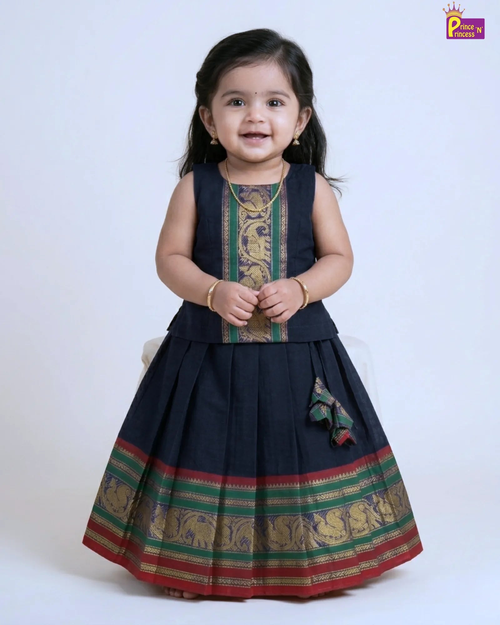 Child wearing a traditional navy blue dress with green and red patterns on a white background