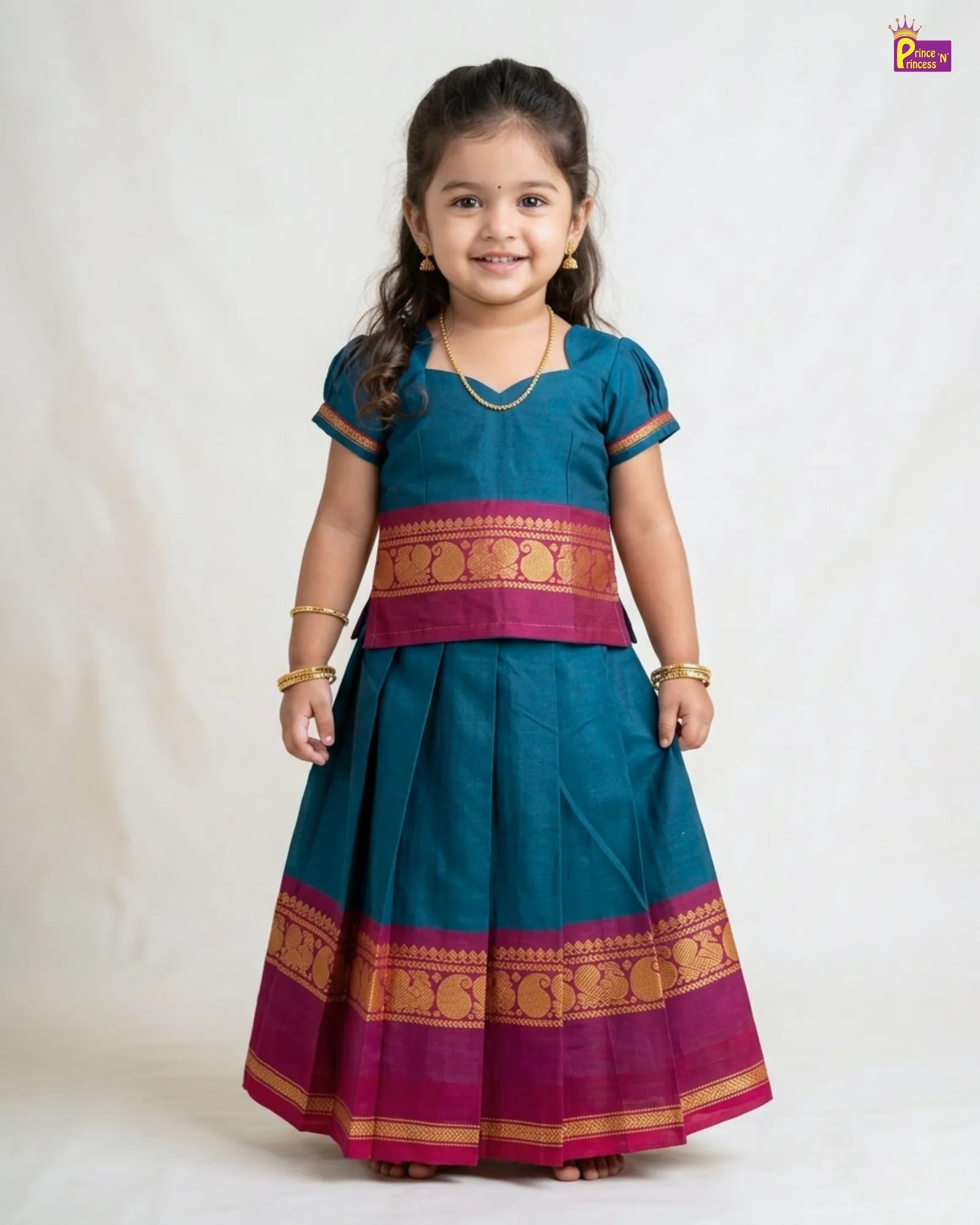 Young girl wearing a traditional teal and pink outfit with gold patterns on a white background