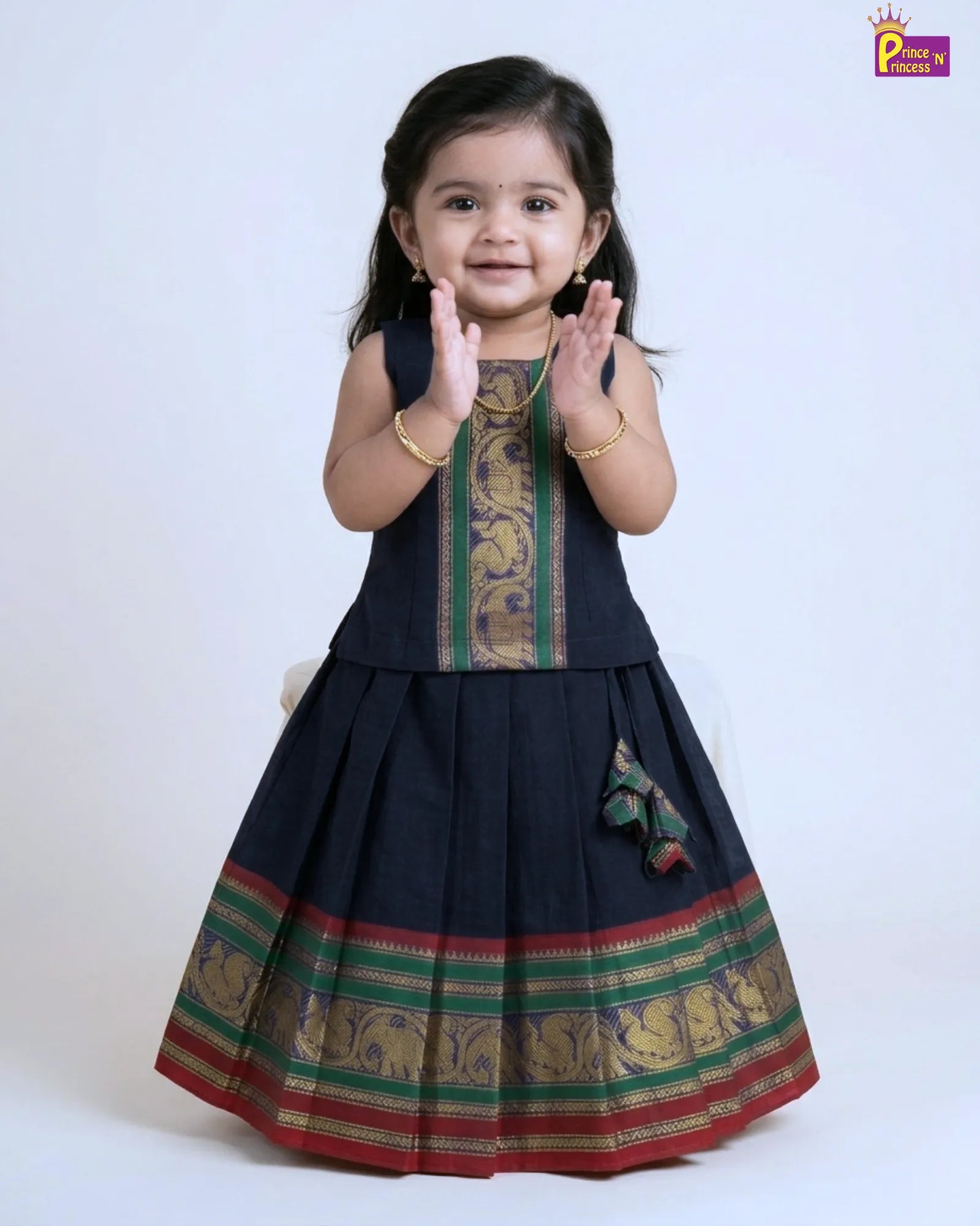Child wearing a traditional black dress with green and red patterns on a white background